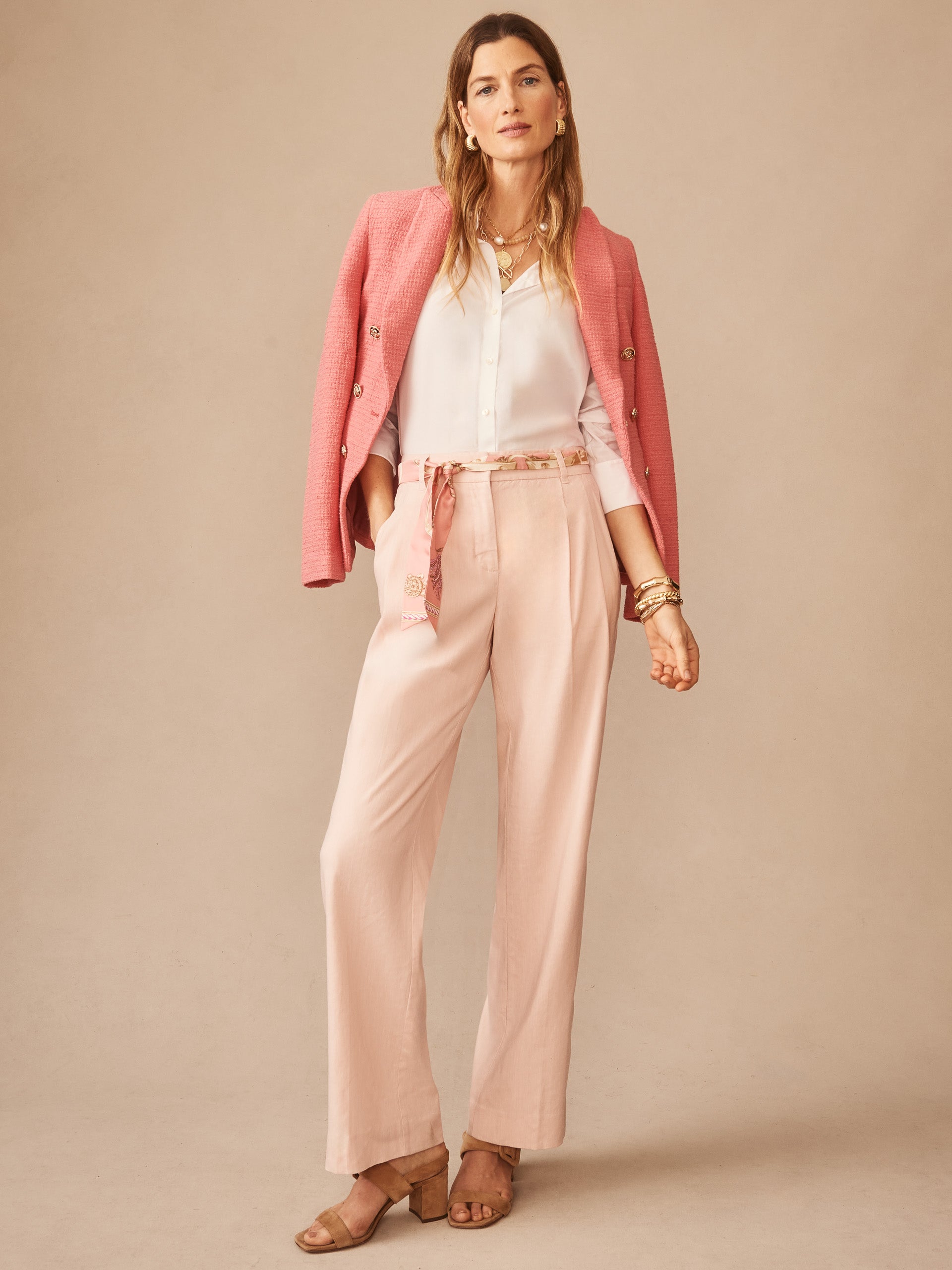 Woman wearing J.McLaughlin Fiona Linen Blend Pants styled with a white blouse and pink blazer draped over shoulders, embodying effortlessly stylish, enduring designs with innovative fabrics.