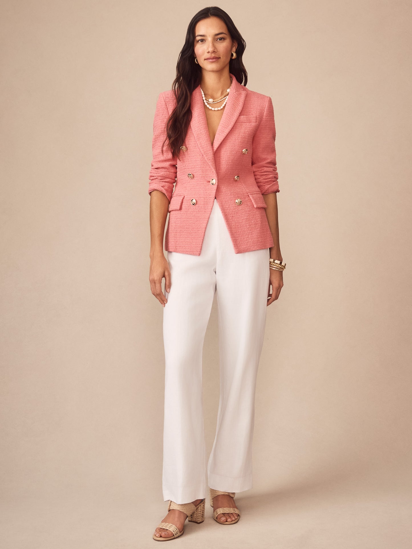 Woman wearing Genevieve Cotton Bouclé Blazer in soft pink by J.McLaughlin, styled with white pants and layered pearl necklaces, showcasing effortlessly stylish, enduring designs.