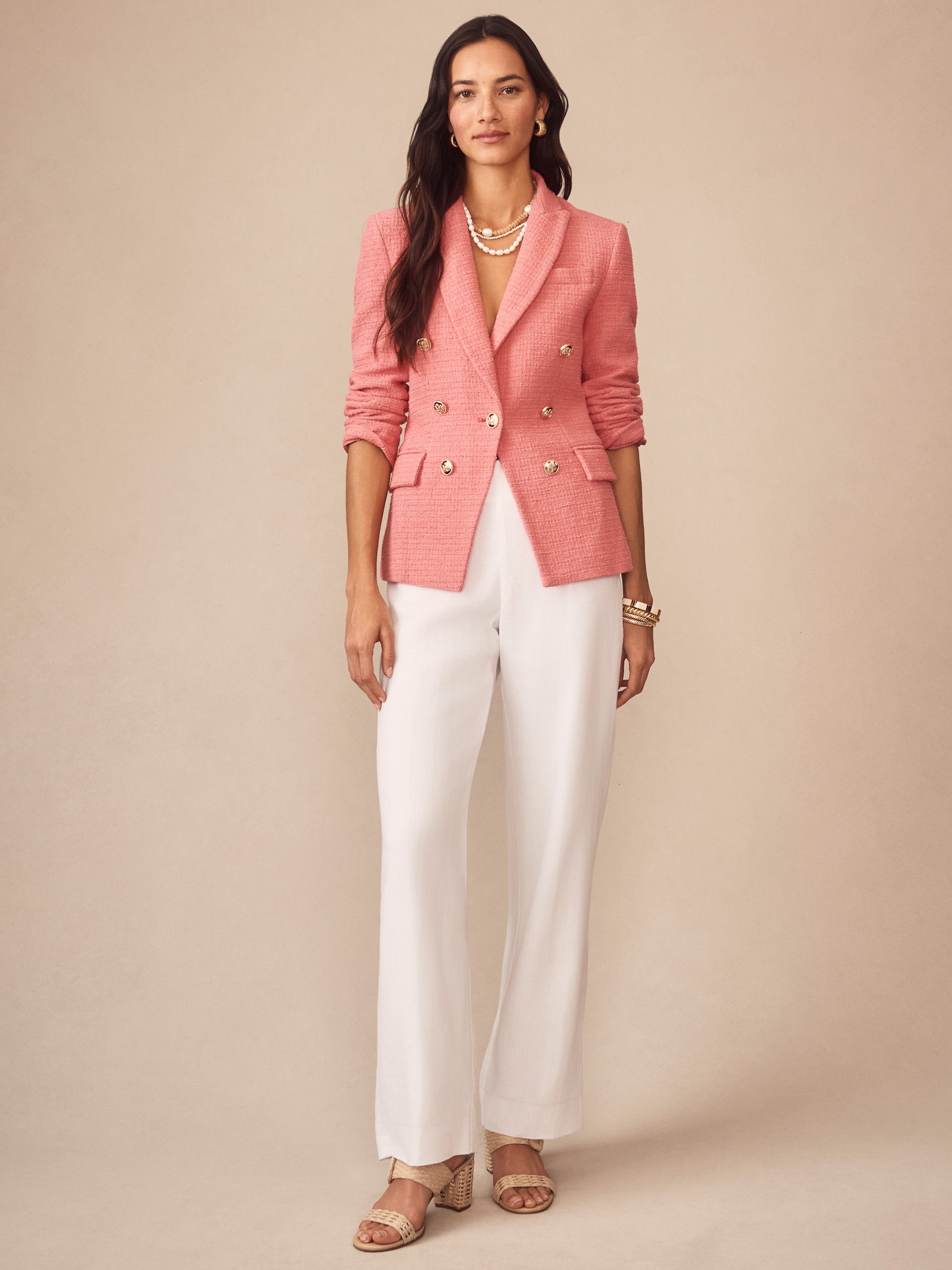 Woman wearing Genevieve Cotton Bouclé Blazer in soft pink by J.McLaughlin, styled with white pants and layered pearl necklaces, showcasing effortlessly stylish, enduring designs.