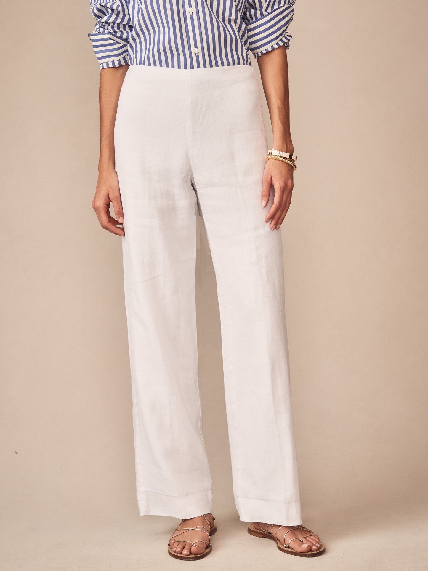 Woman wearing J.McLaughlin Carter Linen Pants in white paired with a blue and white striped shirt and sandals, showcasing effortlessly stylish, enduring designs with a legacy of timeless fashion.
