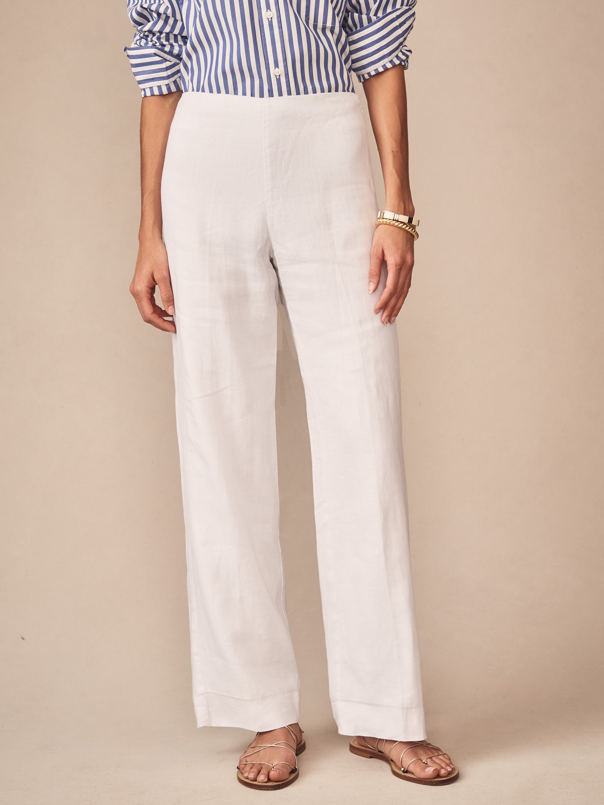 Woman wearing J.McLaughlin Carter Linen Pants in white paired with a blue and white striped shirt and sandals, showcasing effortlessly stylish, enduring designs with a legacy of timeless fashion.