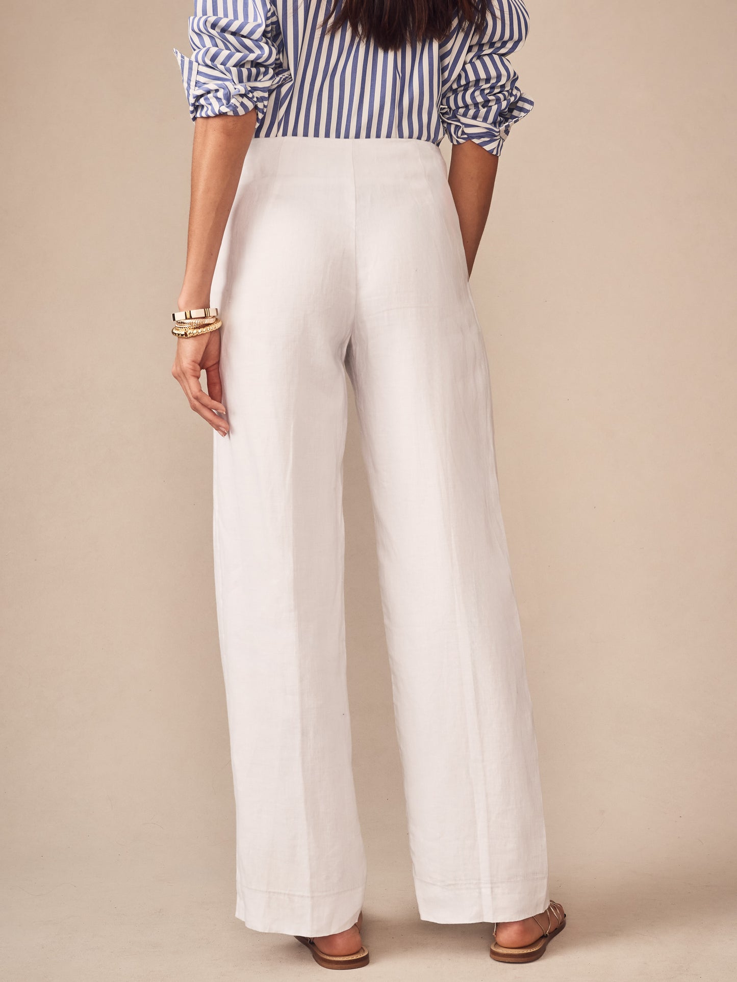 Back view of a woman wearing Carter Linen Pants in white, styled with a blue and white striped blouse and gold bangles, showcasing J.McLaughlin’s effortlessly stylish, enduring designs.