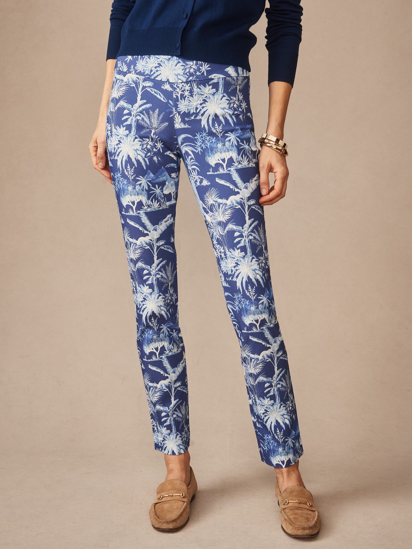 Woman wearing Masie Pants in Garden Isle featuring a blue and white tropical pattern, styled with a navy sweater and tan loafers, exemplifying J.McLaughlin’s effortlessly stylish, enduring designs and innovative fabrics, a destination for defining style. Life, Well-Lived.