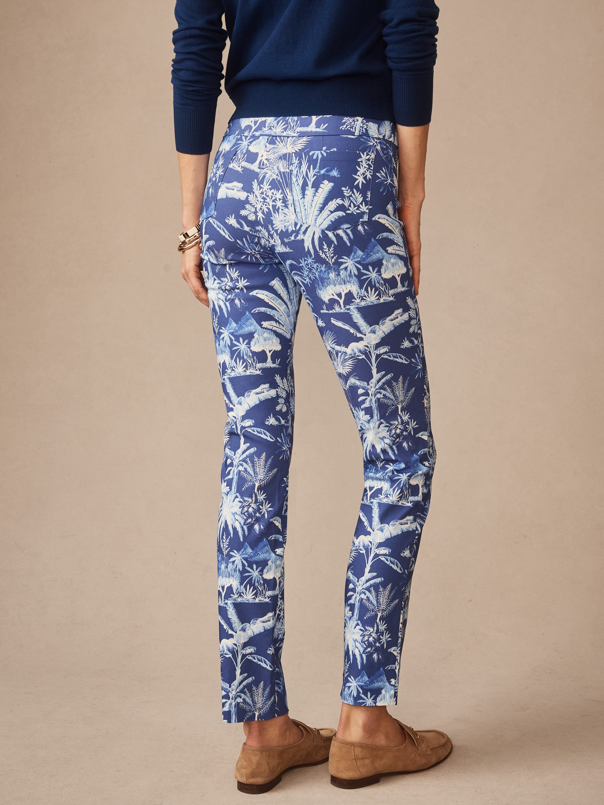 Woman wearing Masie Pants in Garden Isle by J.McLaughlin, featuring a blue tropical print paired with a navy top and brown loafers, showcasing effortlessly stylish, enduring designs and innovative fabrics.
