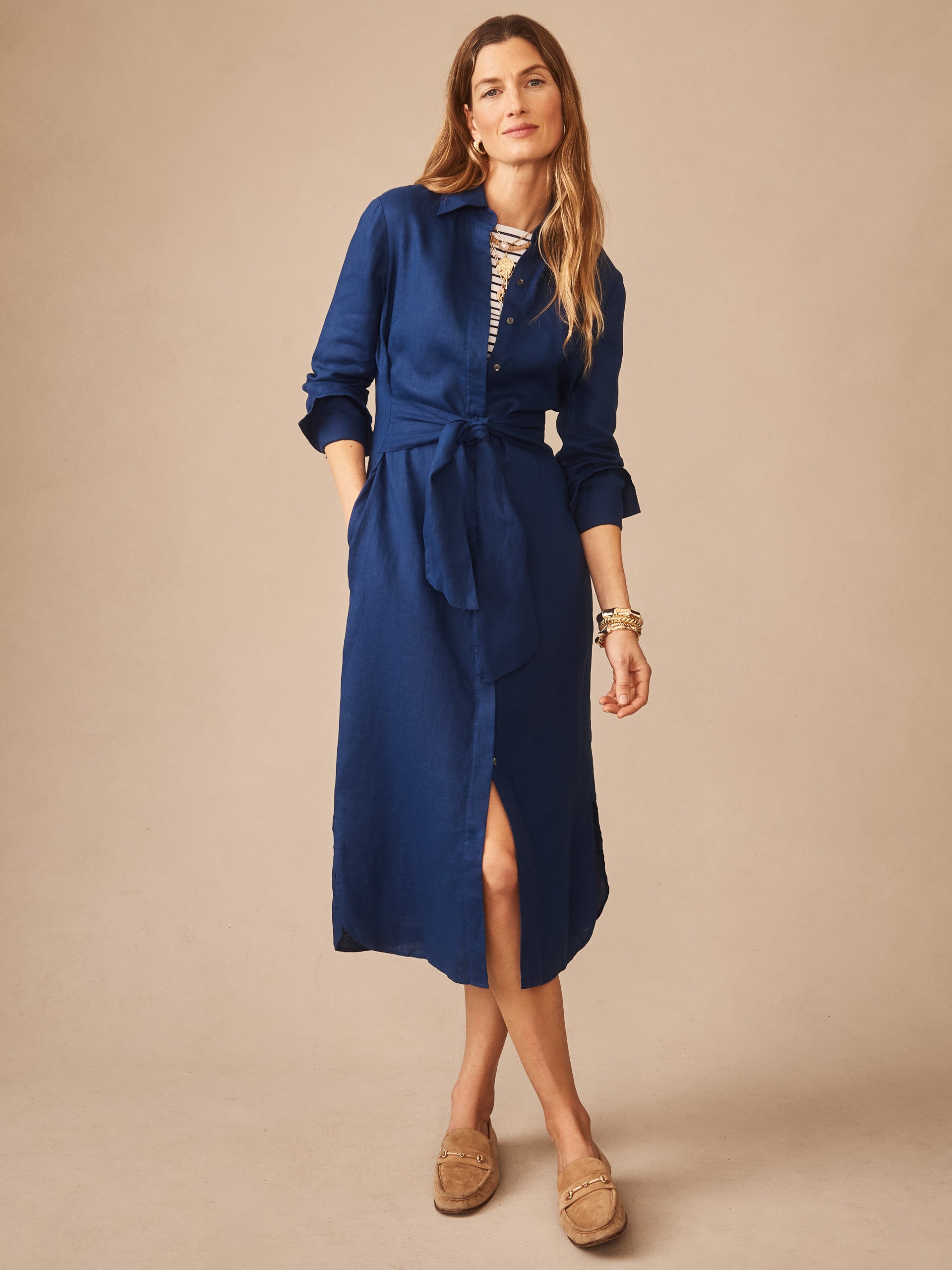 Woman wearing a navy blue Orla Linen Dress by J.McLaughlin with a tied waist, button-down front, and rolled sleeves, showcasing effortlessly stylish enduring designs.