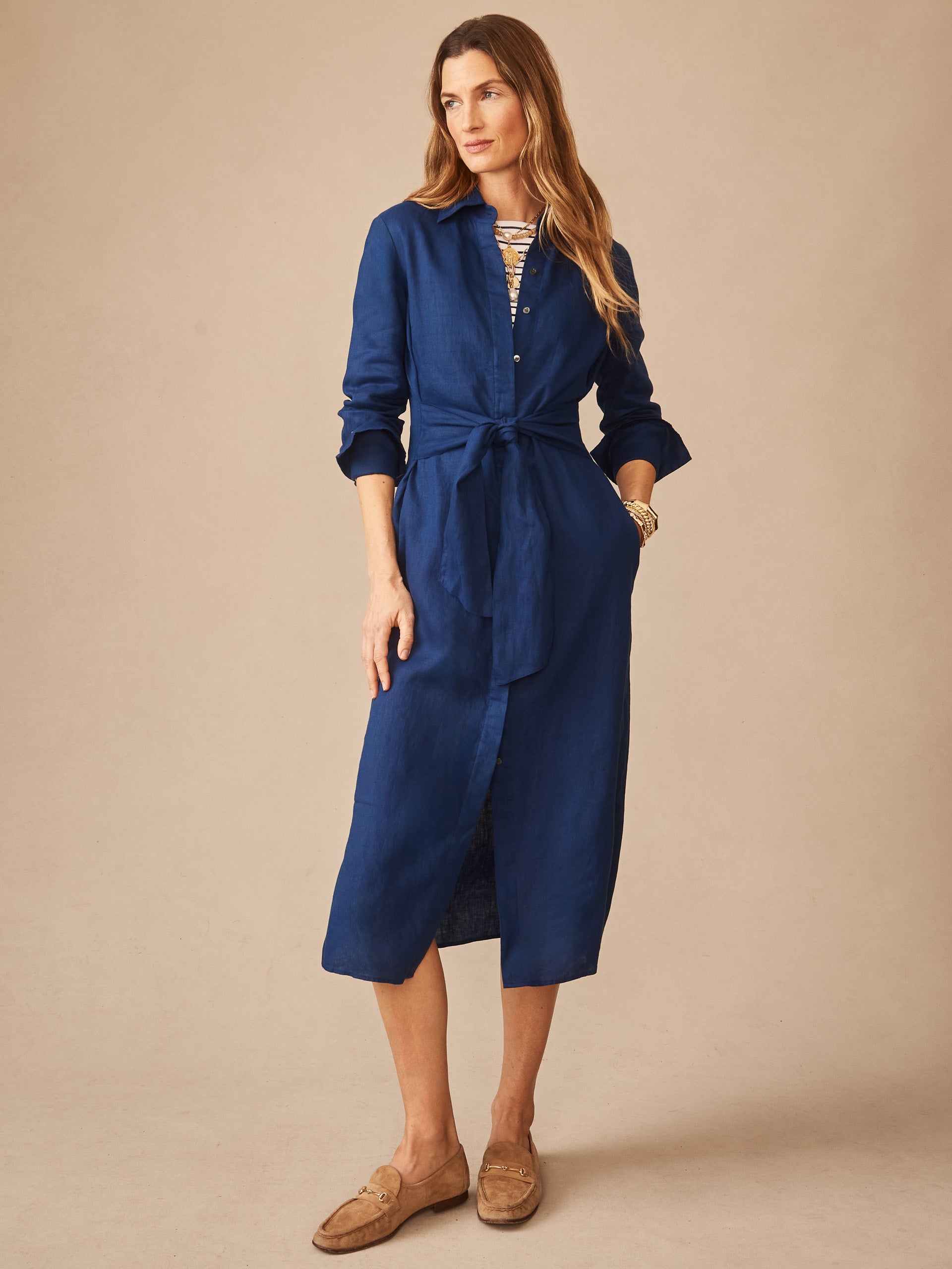 Woman wearing a navy blue Orla Linen Dress by J.McLaughlin, featuring a tie waist and button-down front, embodying effortlessly stylish and enduring designs with innovative fabrics.