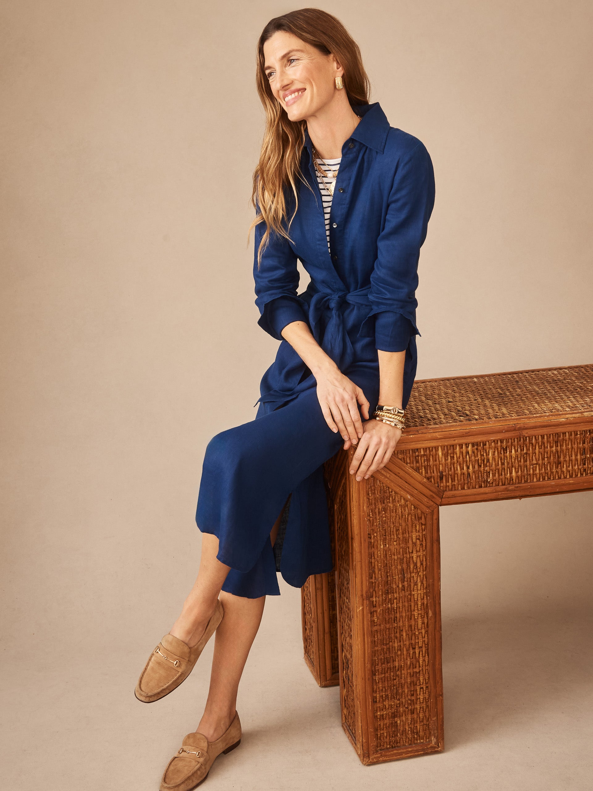 Woman wearing a navy Orla Linen Dress by J.McLaughlin with rolled sleeves and a tied waist, paired with beige loafers, embodying effortlessly stylish, enduring designs and innovative fabrics.