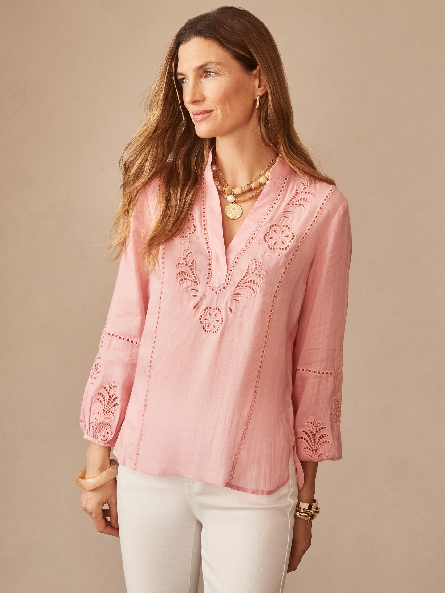 Woman wearing a pink Varsha Blouse by J.McLaughlin featuring delicate embroidery and openwork details, paired with white pants, embodying effortlessly stylish, enduring designs.
