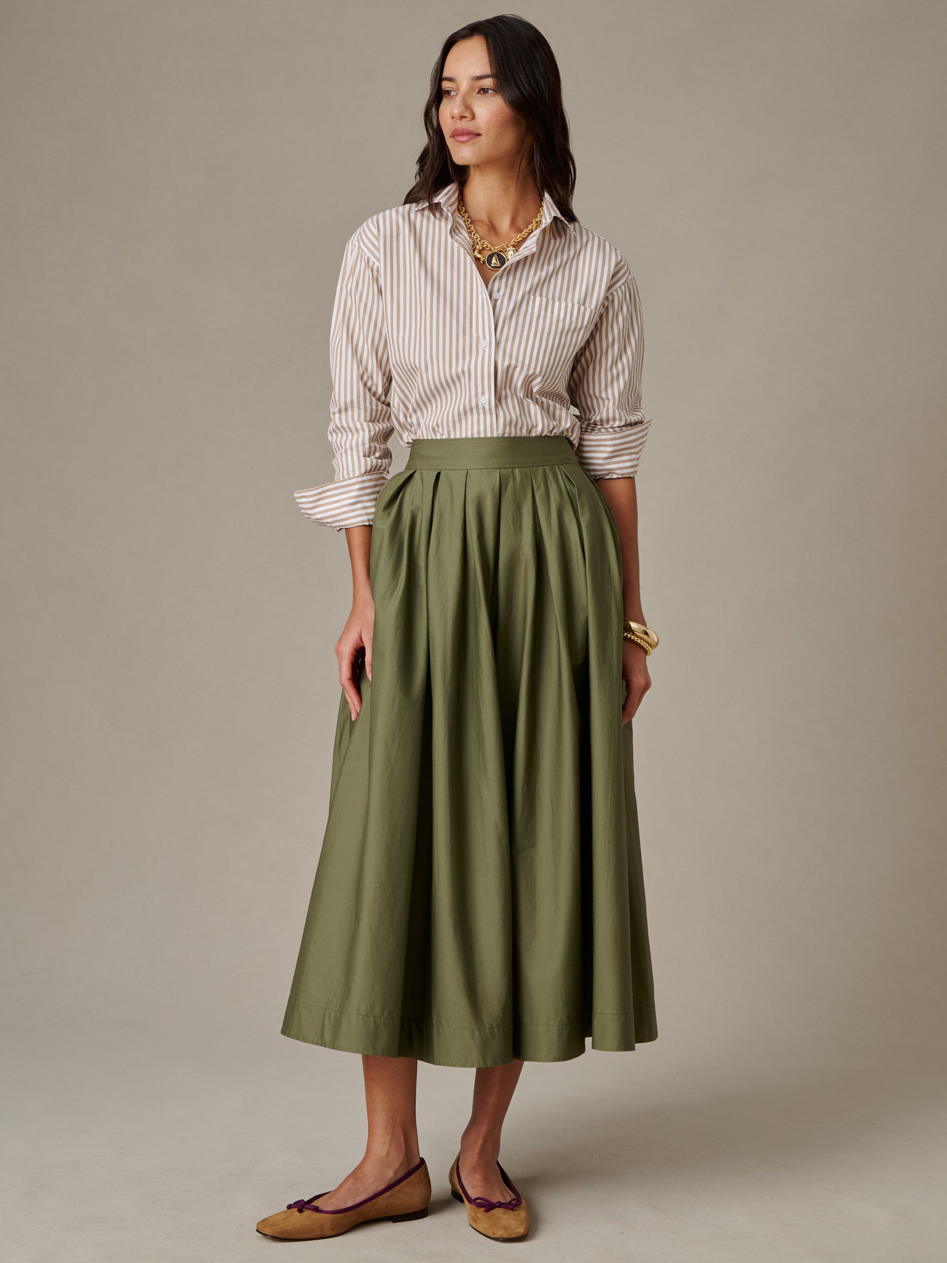 Woman wearing a striped button-down shirt paired with an olive green Arabella Skirt by J.McLaughlin, showcasing an effortlessly stylish and timeless look.