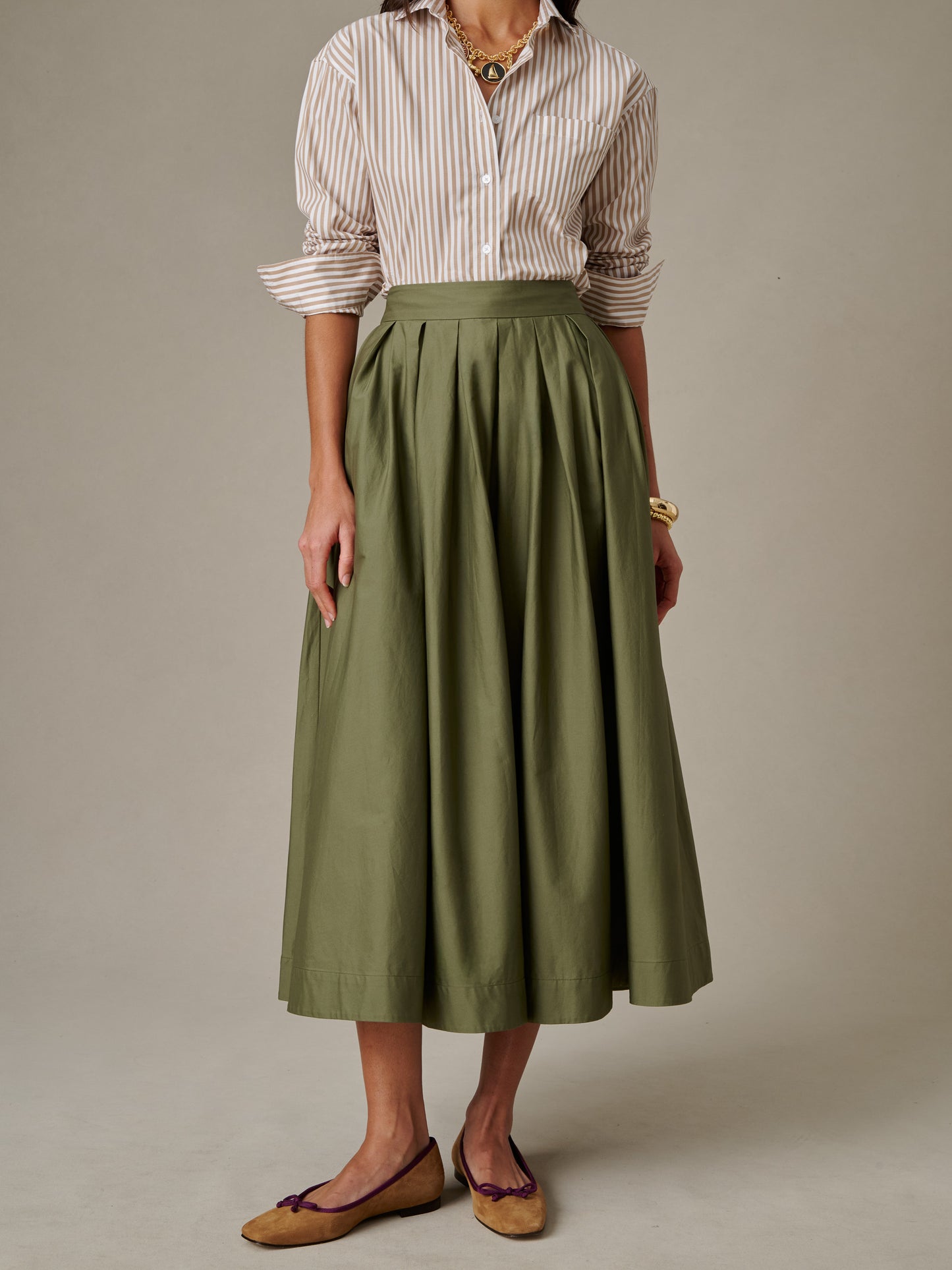 Woman wearing a J.McLaughlin Arabella Skirt in olive green paired with a striped shirt and classic flats, showcasing timeless style and enduring design.