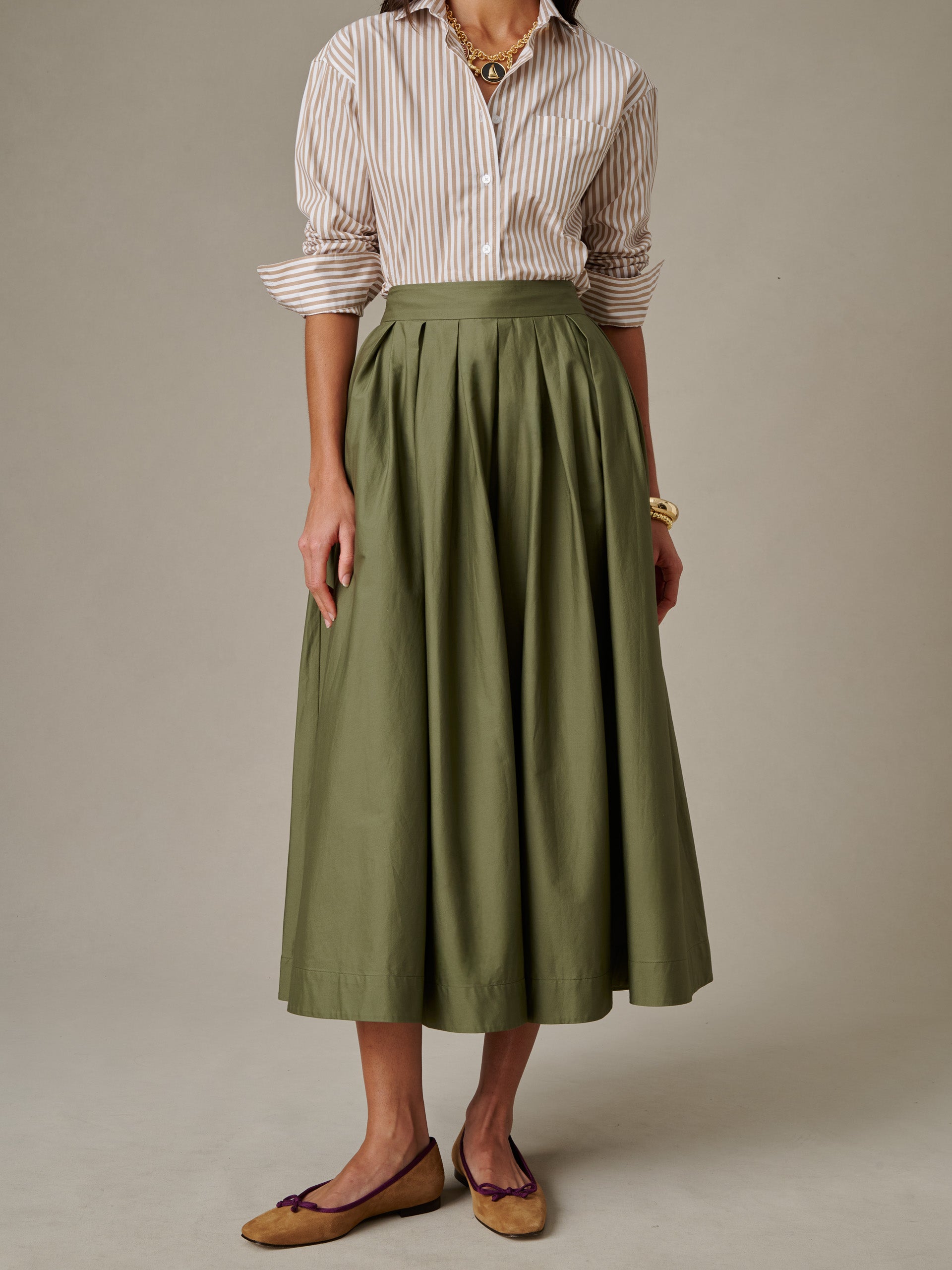 Woman wearing a J.McLaughlin Arabella Skirt in olive green paired with a striped shirt and classic flats, showcasing timeless style and enduring design.
