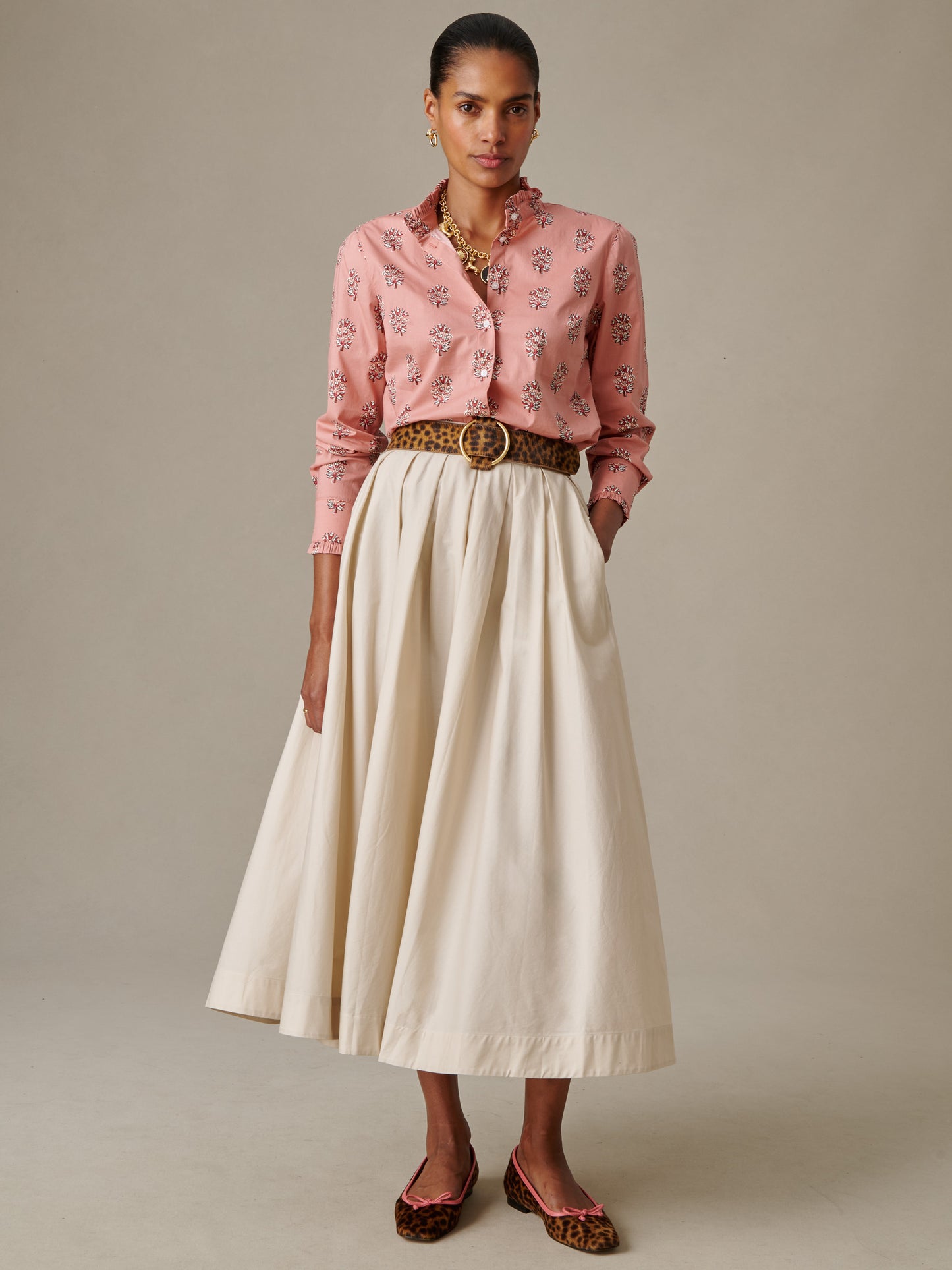 Woman wearing a flowing cream-colored Arabella Skirt by J.McLaughlin paired with a pink patterned blouse, leopard print belt, and matching leopard print flats, showcasing effortlessly stylish timeless fashion.