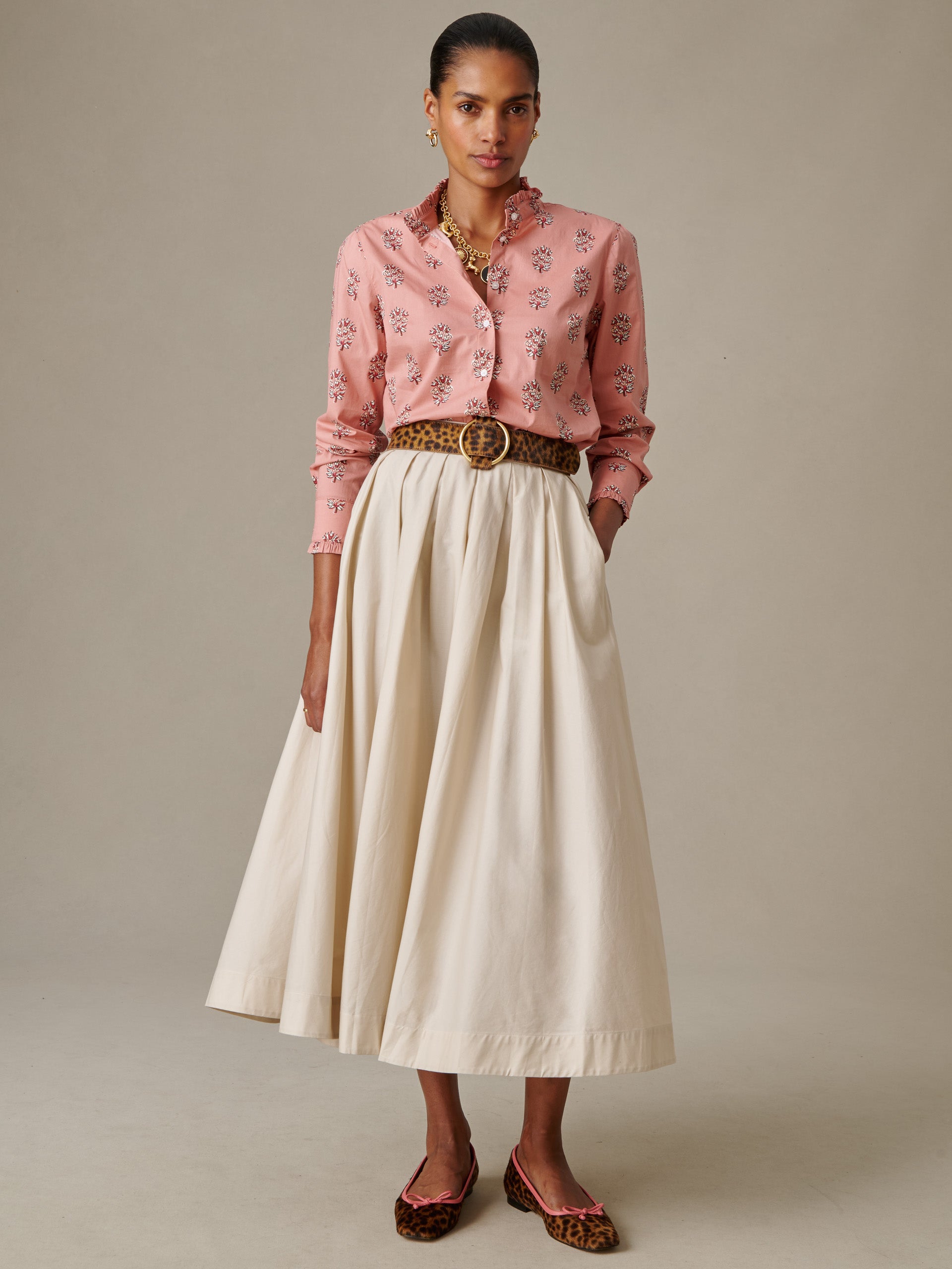 Woman wearing a flowing cream-colored Arabella Skirt by J.McLaughlin paired with a pink patterned blouse, leopard print belt, and matching leopard print flats, showcasing effortlessly stylish timeless fashion.