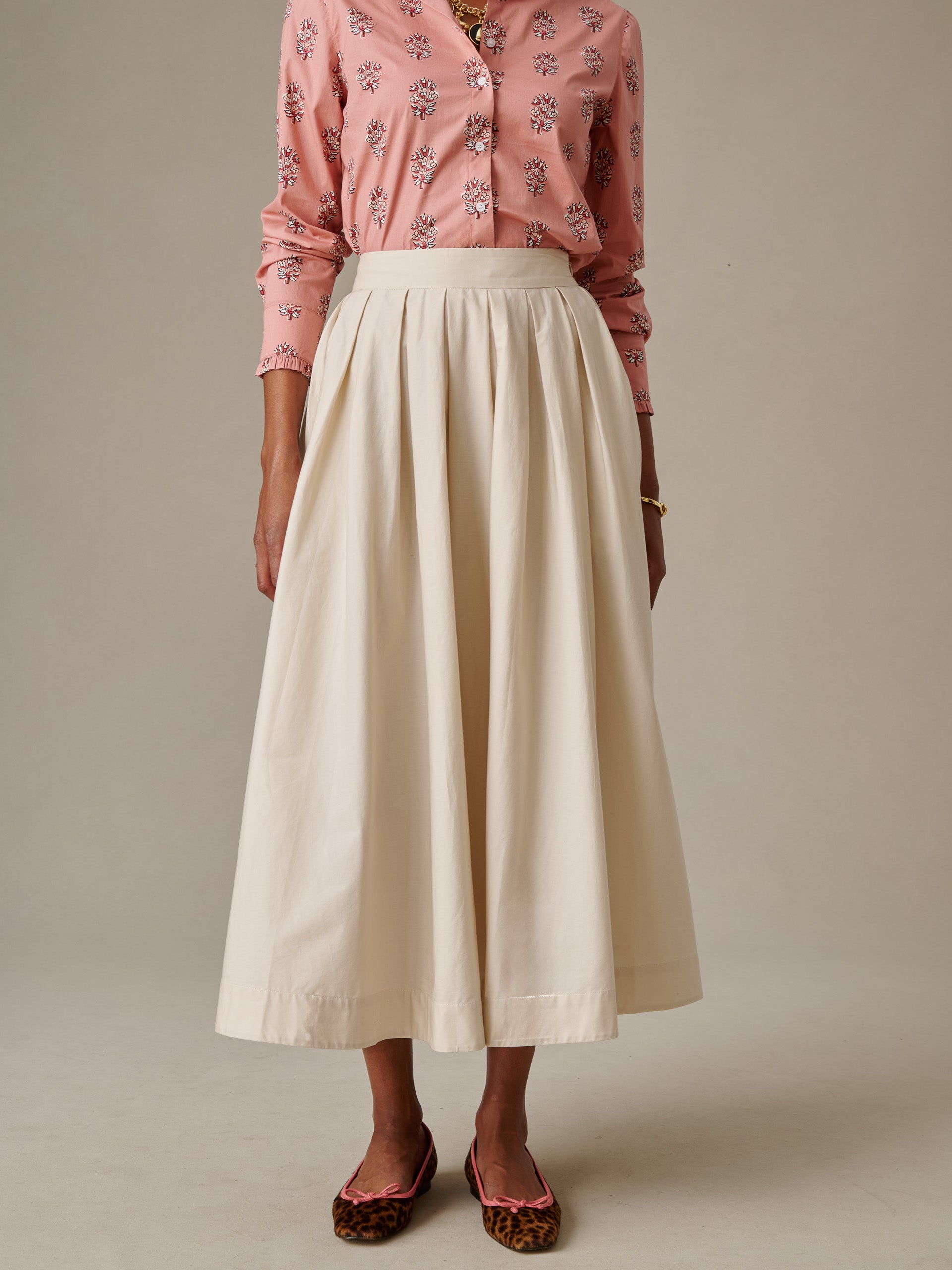 Woman wearing a cream-colored Arabella Skirt paired with a floral pink blouse and leopard print flats, showcasing J.McLaughlin’s timeless style and craftsmanship.