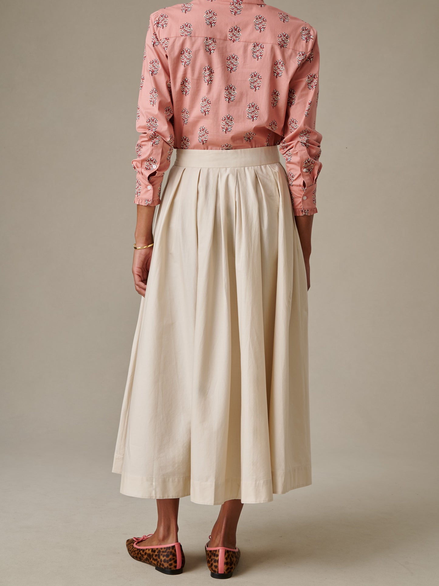 Woman wearing an ivory Arabella Skirt by J.McLaughlin paired with a pink floral blouse and leopard print flats, showcasing timeless style and enduring design.
