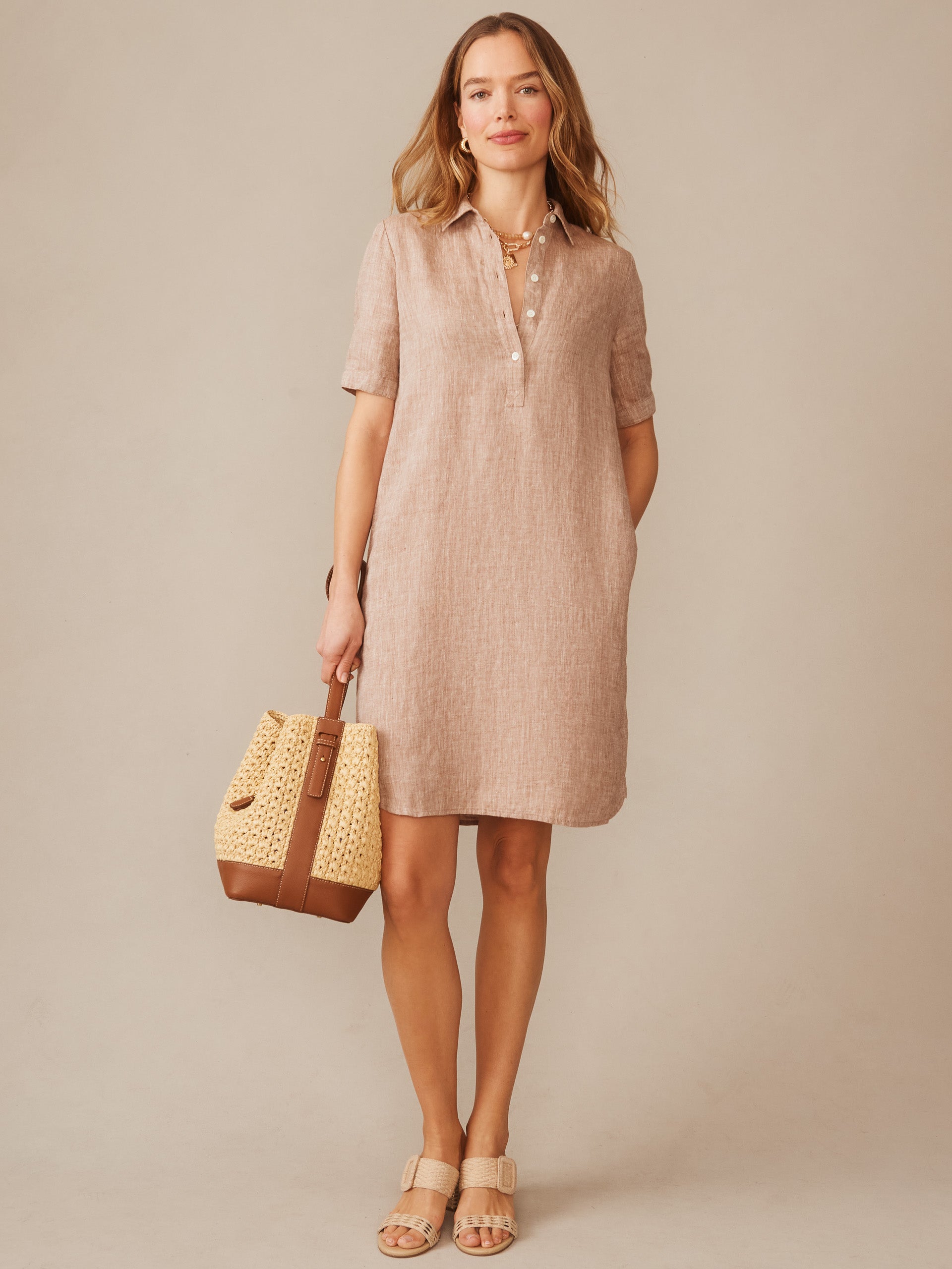 Woman wearing an Arissa Linen Dress by J.McLaughlin in a soft latte tone, paired with a woven bag and sandals, showcasing effortlessly stylish, enduring designs for a life well-lived.