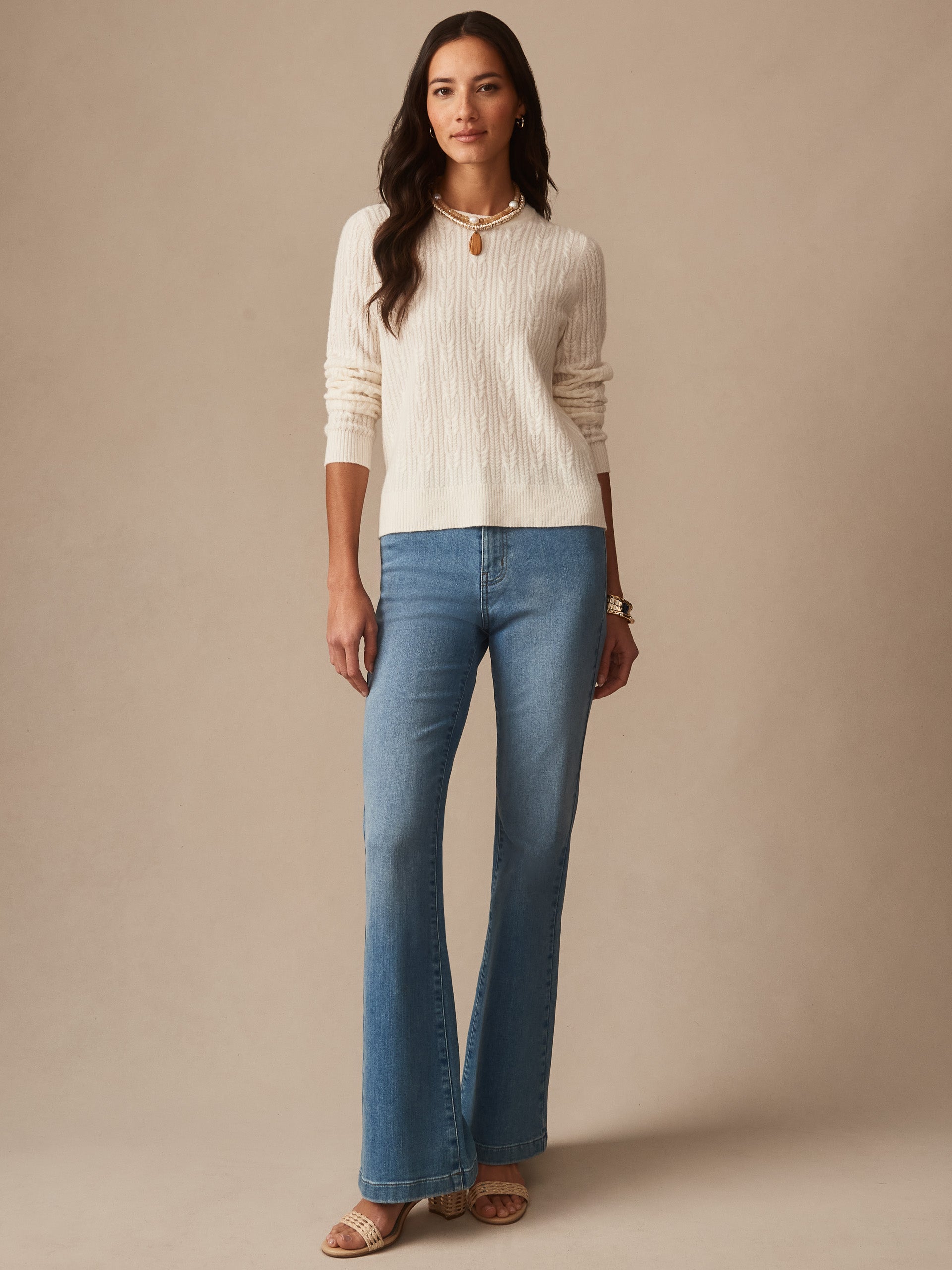 Woman wearing an ivory Ashby Cashmere Sweater by J.McLaughlin paired with blue flared jeans and beige sandals, showcasing effortlessly stylish, enduring designs and innovative fabrics.