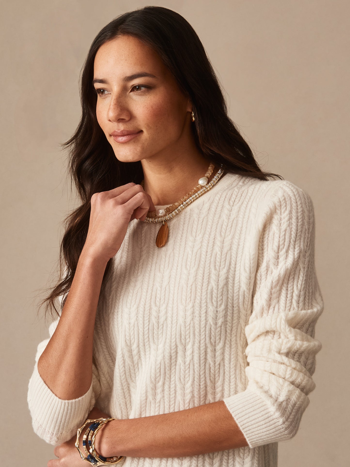 Woman wearing an ivory Ashby Cashmere Sweater by J.McLaughlin with layered necklaces and bracelets, showcasing effortlessly stylish, enduring designs and innovative fabrics.