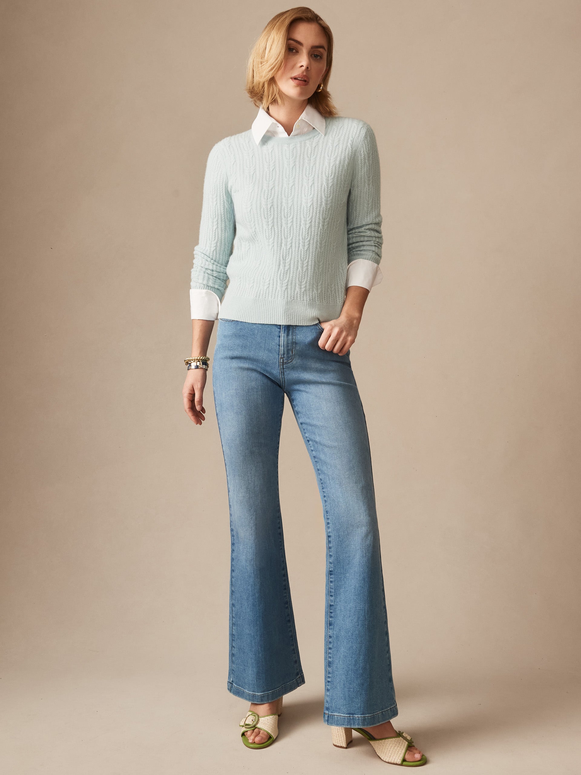 Woman wearing a soft aqua Ashby Cashmere Sweater by J.McLaughlin paired with light blue flared jeans and open-toe heels, showcasing effortlessly stylish, enduring designs.