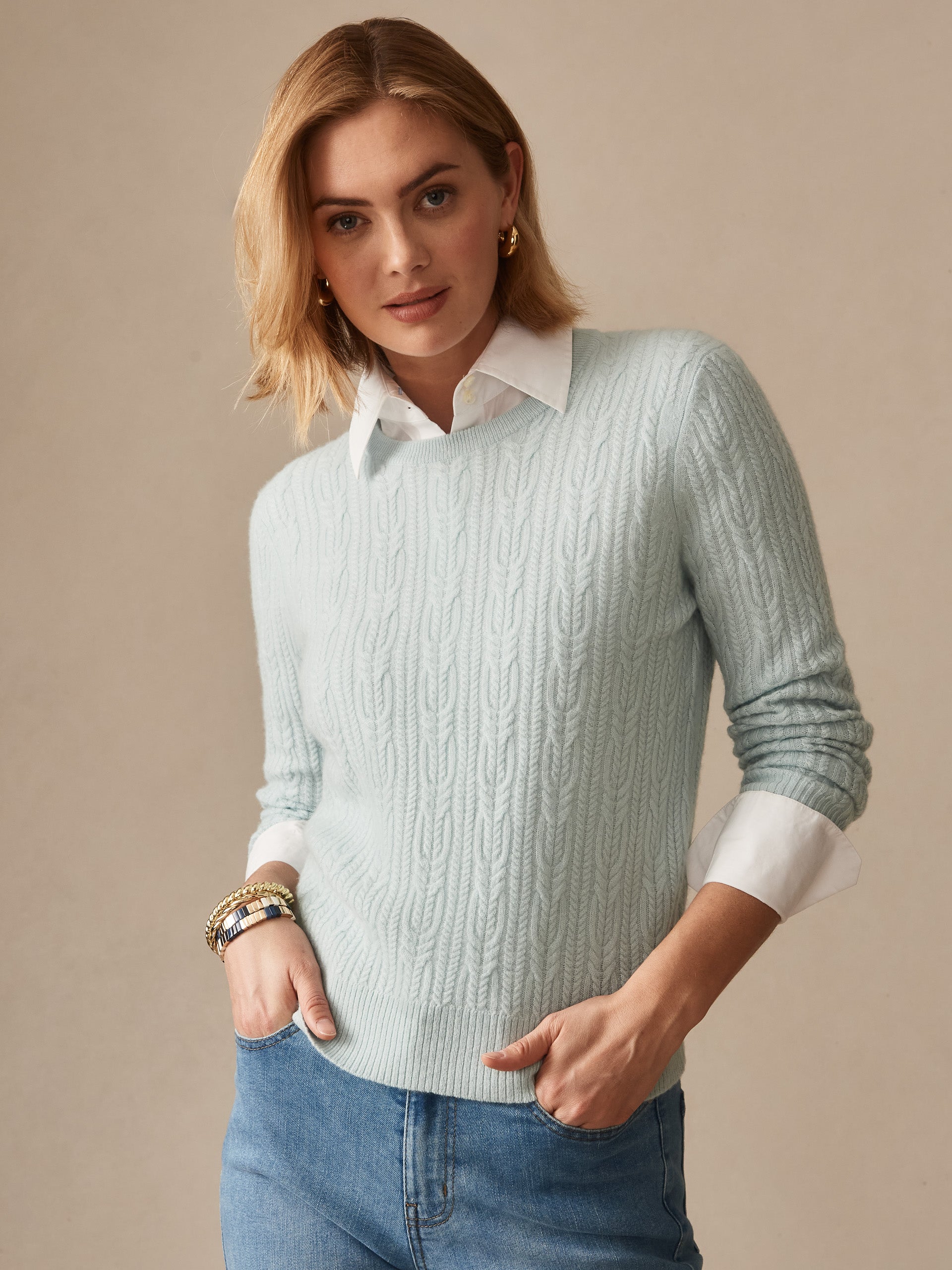 Woman wearing a soft aqua Ashby Cashmere Sweater layered over a white collared shirt with light wash jeans, styled effortlessly by J.McLaughlin for enduring designs and timeless fashion.