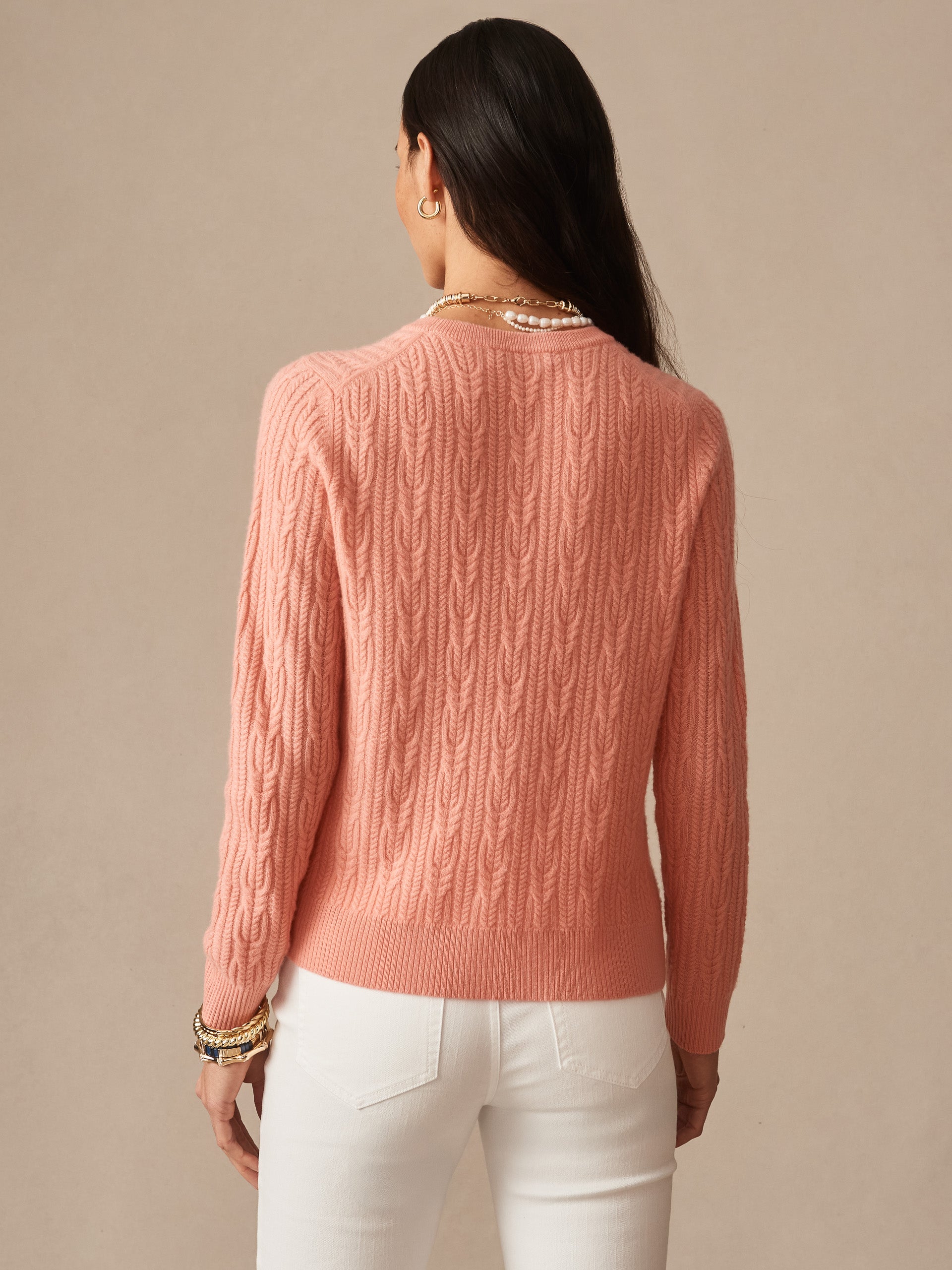 Woman wearing a soft coral Ashby Cashmere Sweater by J.McLaughlin, showcasing a cable knit design that reflects effortlessly stylish, enduring designs and a legacy of timeless fashion.