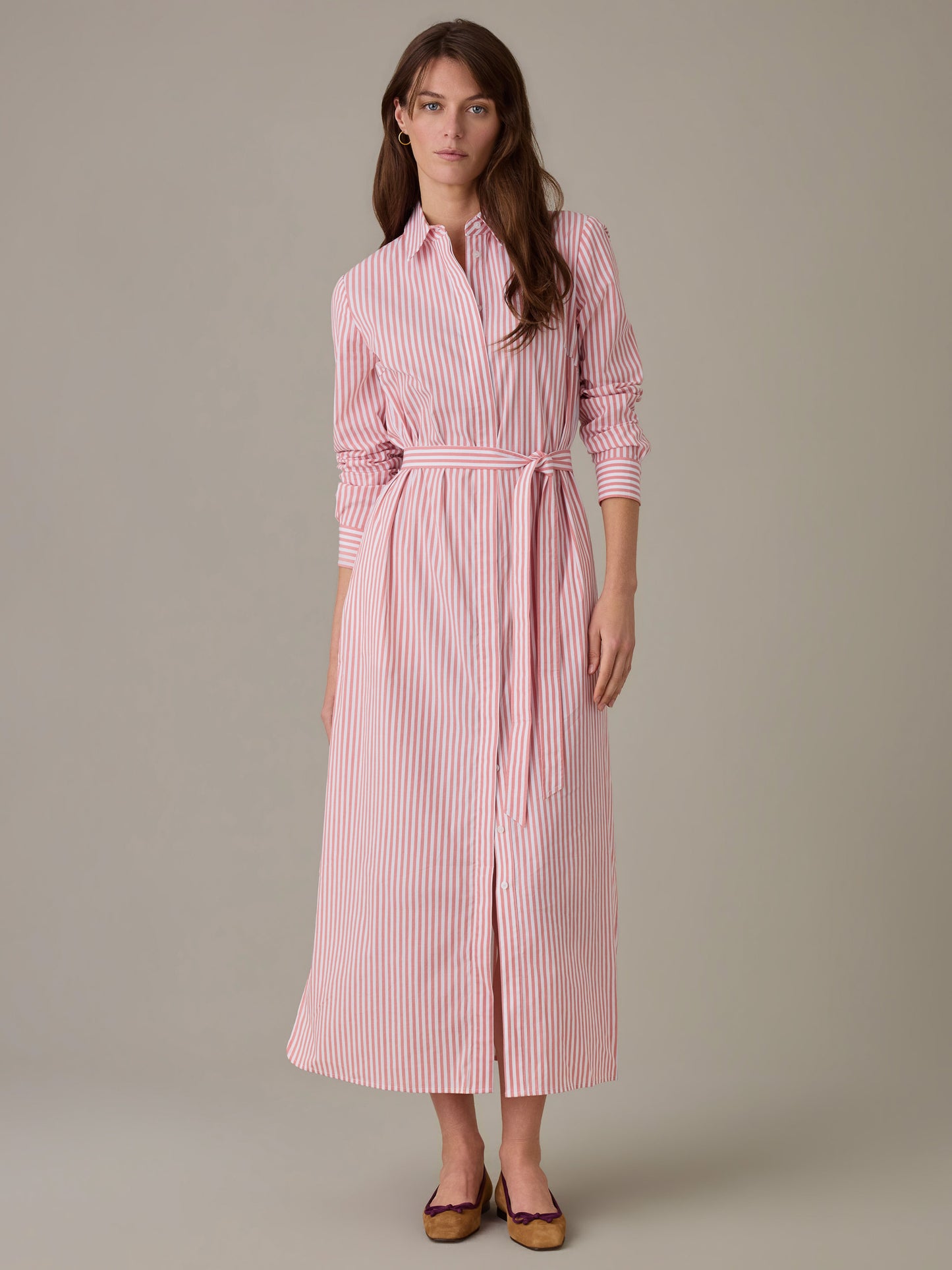 Woman wearing a Leighton Dress in Stripe by J.McLaughlin, featuring a long-sleeve, button-down design with a waist tie in red and white stripes, styled with flats.