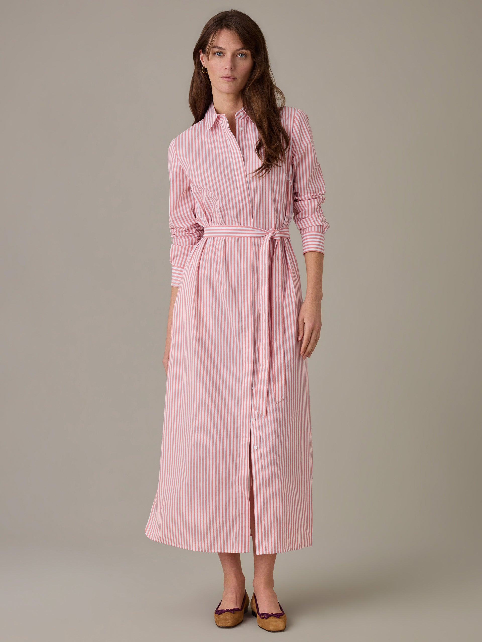 Woman wearing a Leighton Dress in Stripe by J.McLaughlin, featuring a long-sleeve, button-down design with a waist tie in red and white stripes, styled with flats.