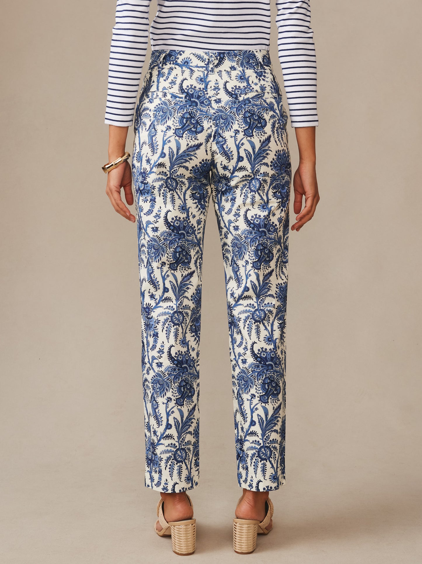 A rear view of a woman wearing Avery Pants in Heirloom Paisley by J.McLaughlin, featuring a blue floral pattern on cream fabric, paired with a striped top and block-heeled sandals, showcasing effortlessly stylish, enduring designs and innovative fabrics at a destination for defining style. Life, Well-Lived.