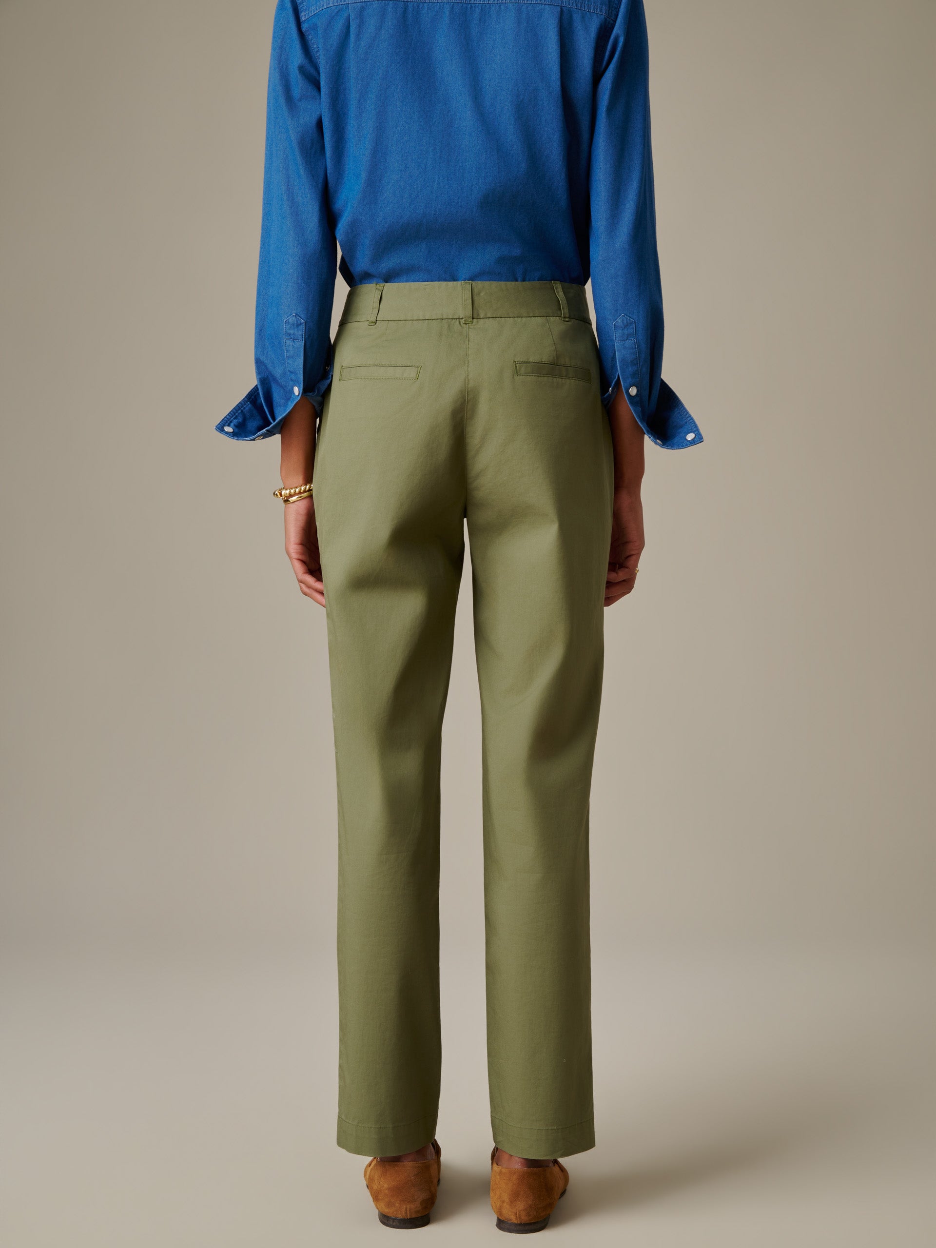 Back view of a person wearing olive green Avery Cotton Chino Pants paired with a blue long-sleeve shirt and brown shoes, showcasing J.McLaughlin's effortless stylish and enduring design.