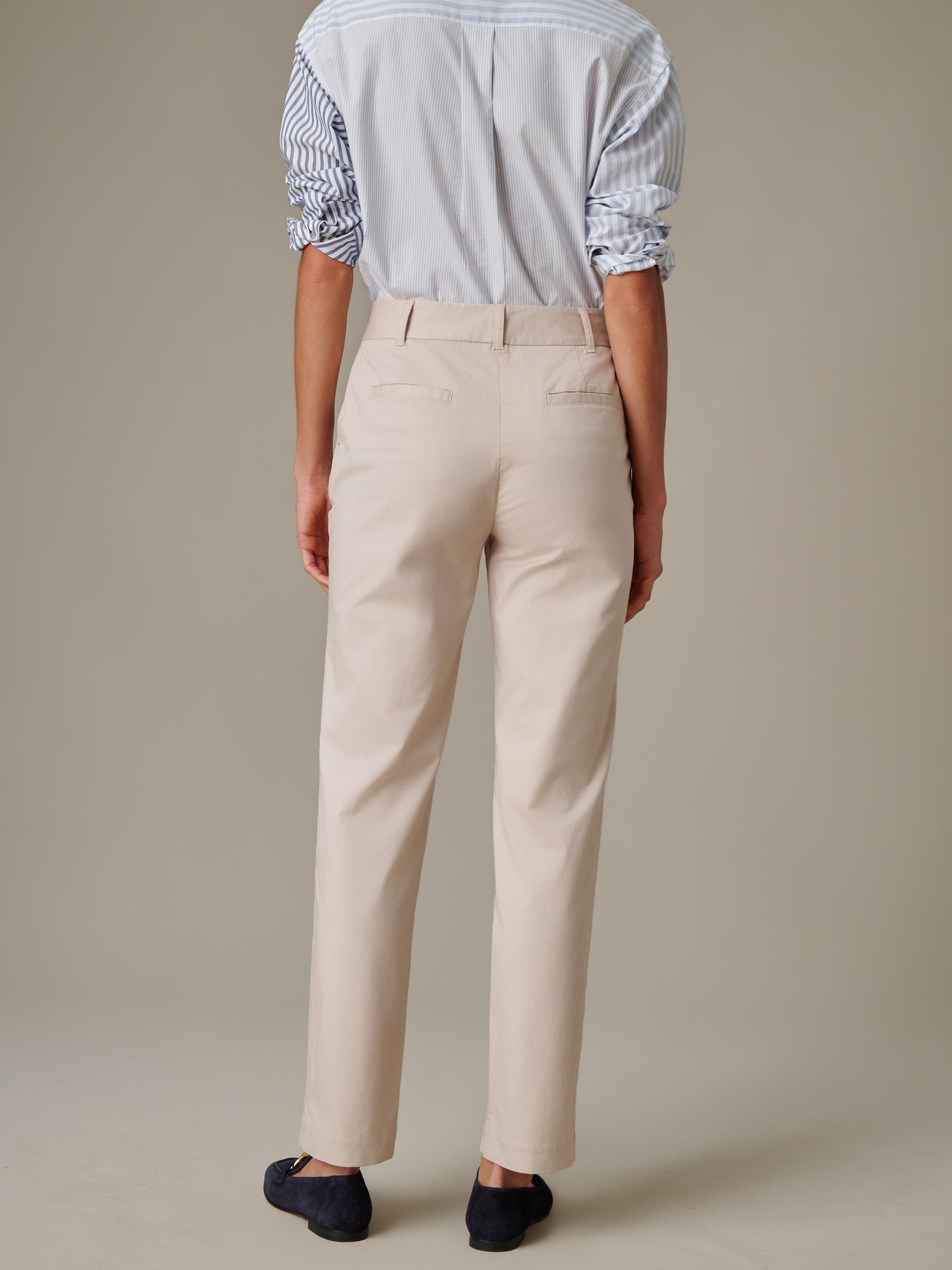 Back view of a person wearing beige Avery Cotton Chino Pants by J.McLaughlin, paired with a striped shirt and navy slip-on shoes, highlighting timeless style and craftsmanship.