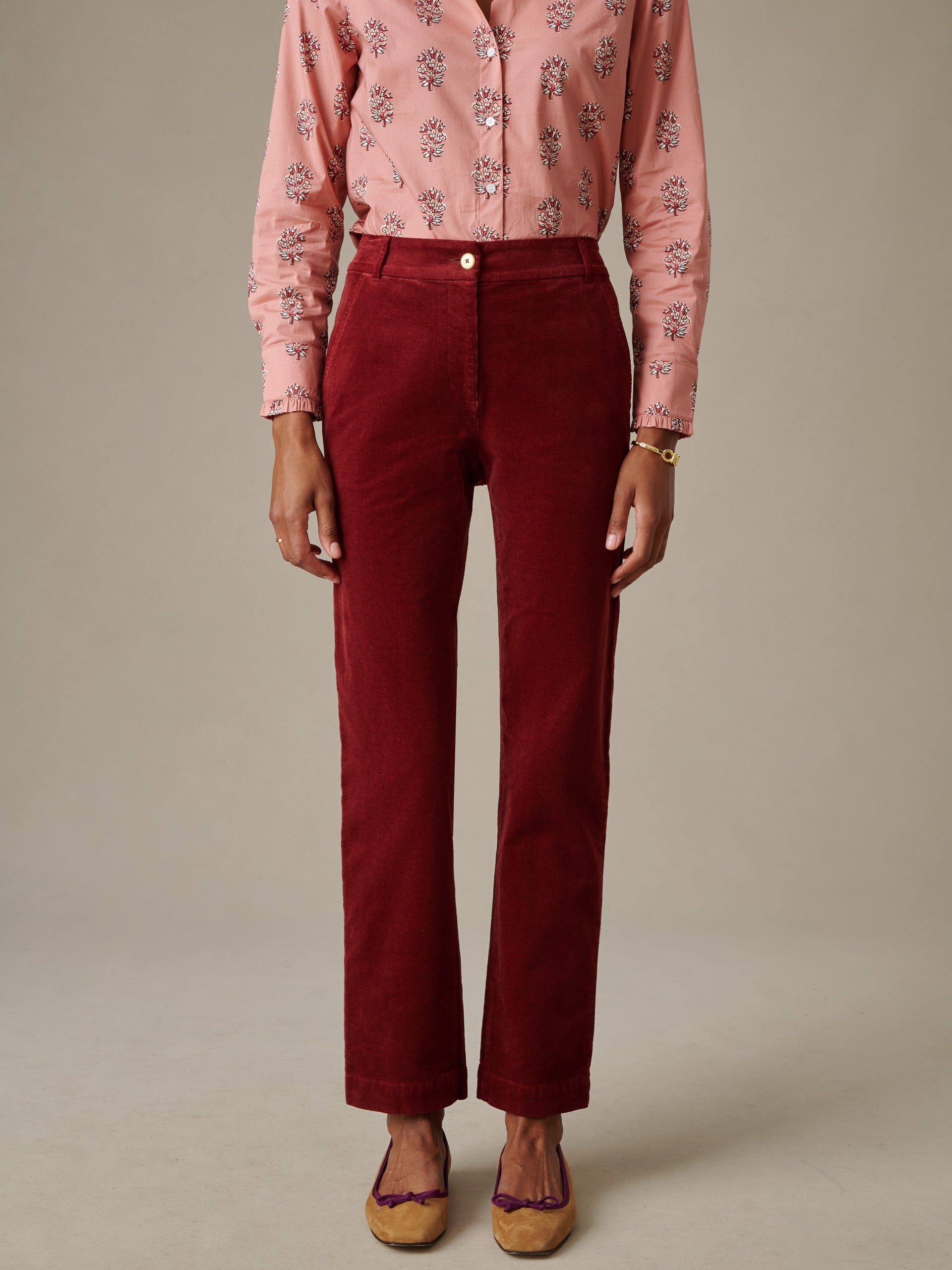 A model wearing deep red Avery Corduroy Pants by J.McLaughlin paired with a patterned pink blouse, showcasing an effortlessly stylish and timeless look.