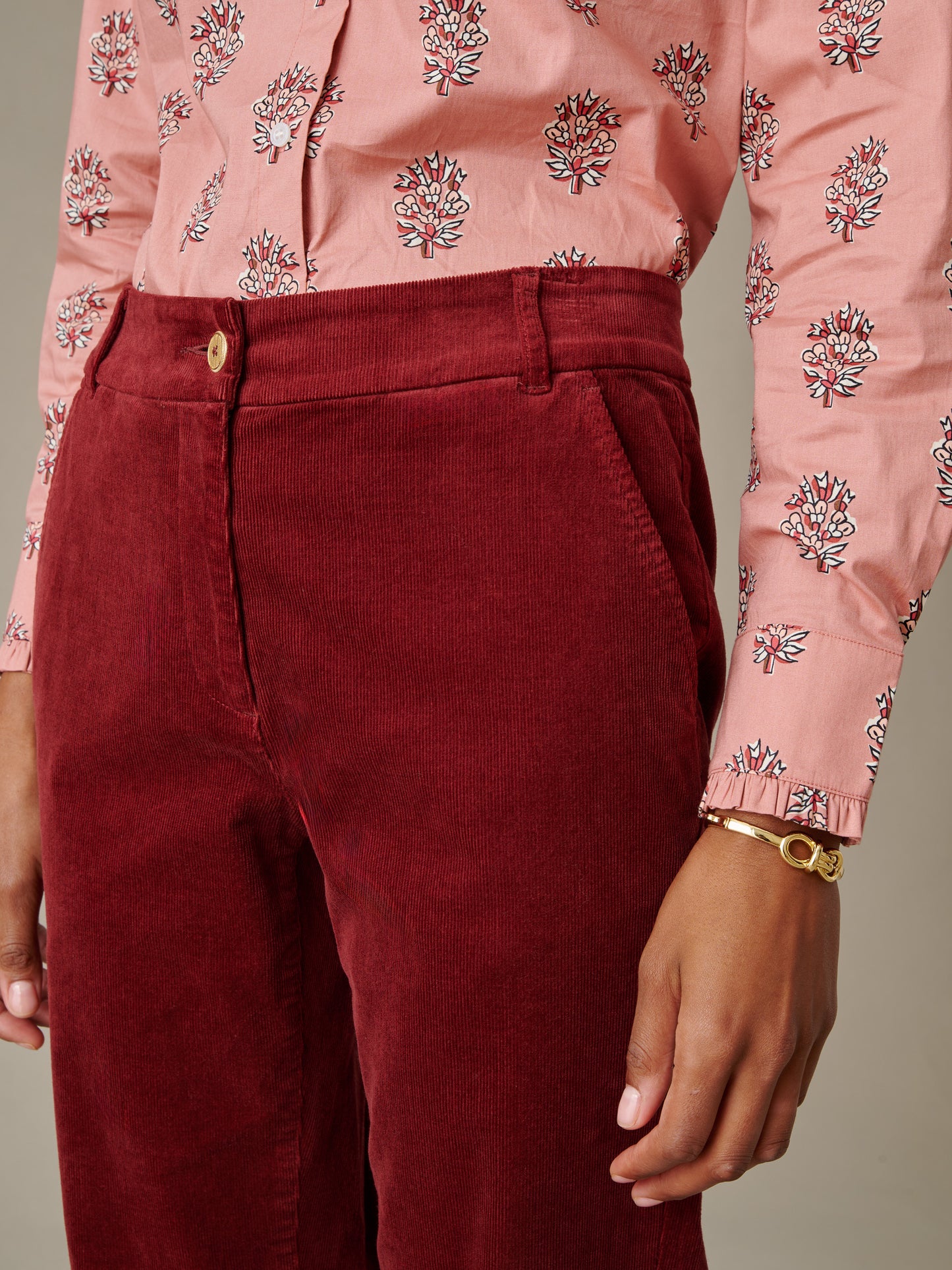 Close-up of a person wearing deep red Avery Corduroy Pants by J.McLaughlin paired with a patterned pink blouse and gold bracelet, showcasing timeless style and craftsmanship.