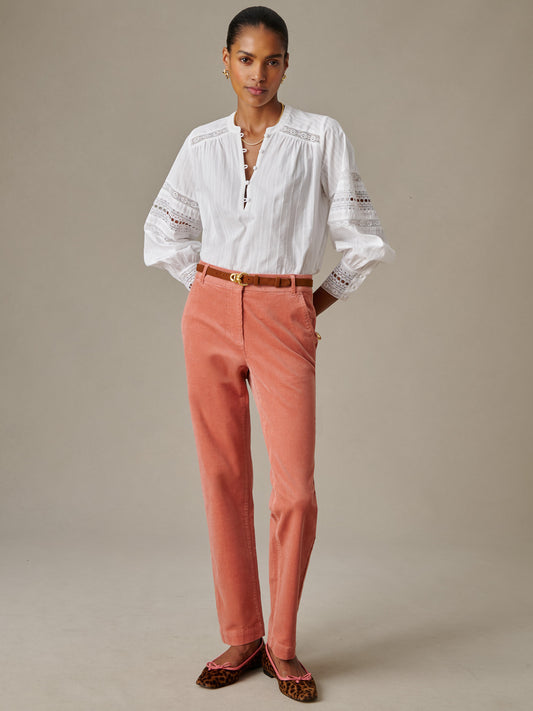 Woman wearing Avery Corduroy Pants by J.McLaughlin in a soft rose tone, paired with a white blouse featuring lace details and a brown belt, showcasing elegant, timeless style.