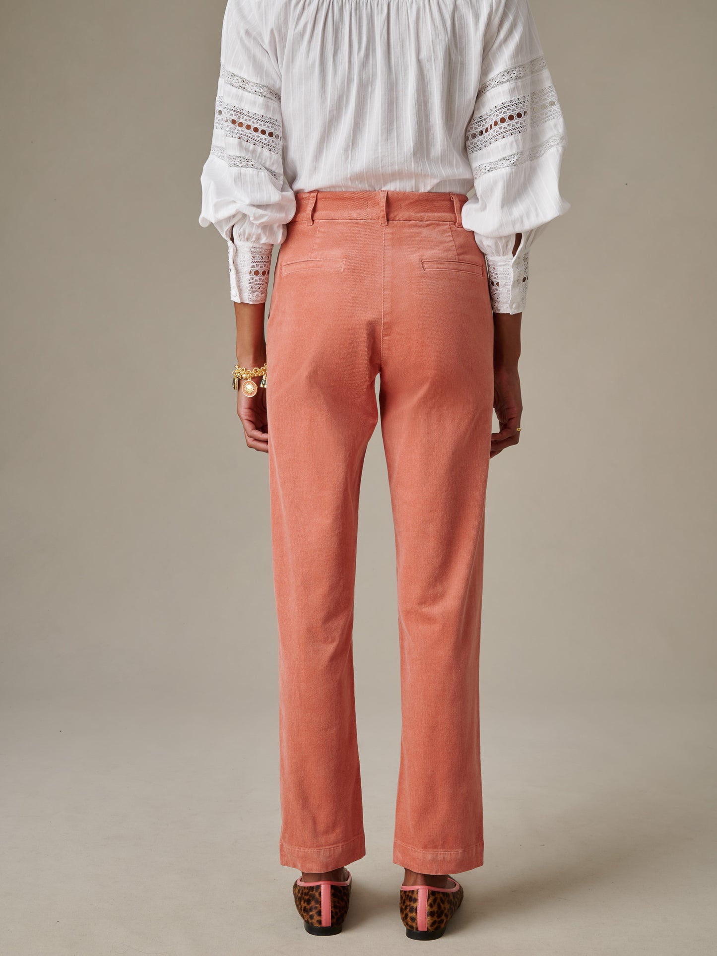 A woman wears Avery Corduroy Pants by J.McLaughlin in a warm coral shade, paired with a detailed white blouse and leopard print heels, showcasing timeless style and enduring design.