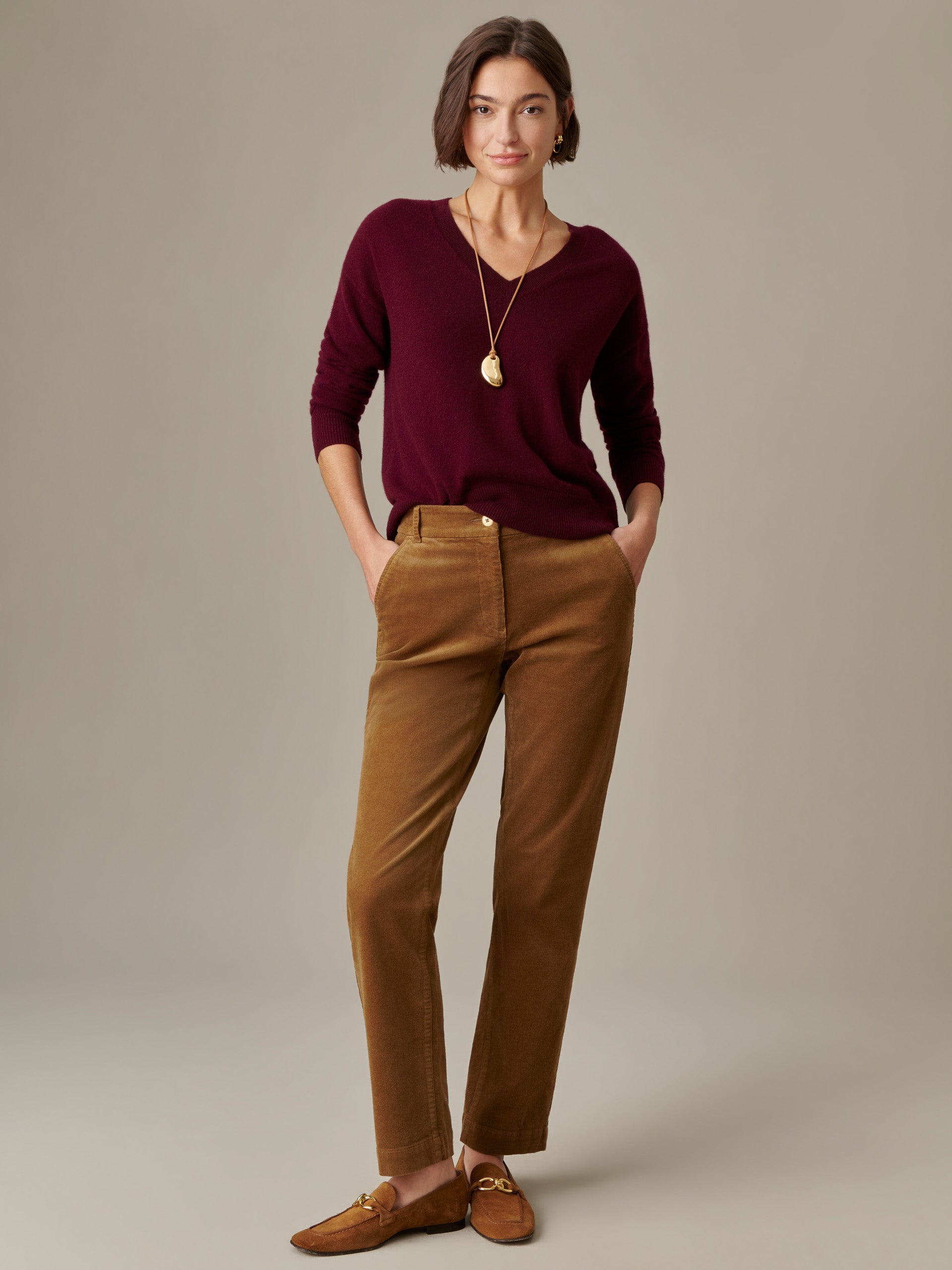 Woman wearing Avery Corduroy Pants by J.McLaughlin in a warm brown shade paired with a deep burgundy sweater and loafers, showcasing an effortlessly stylish, timeless look.