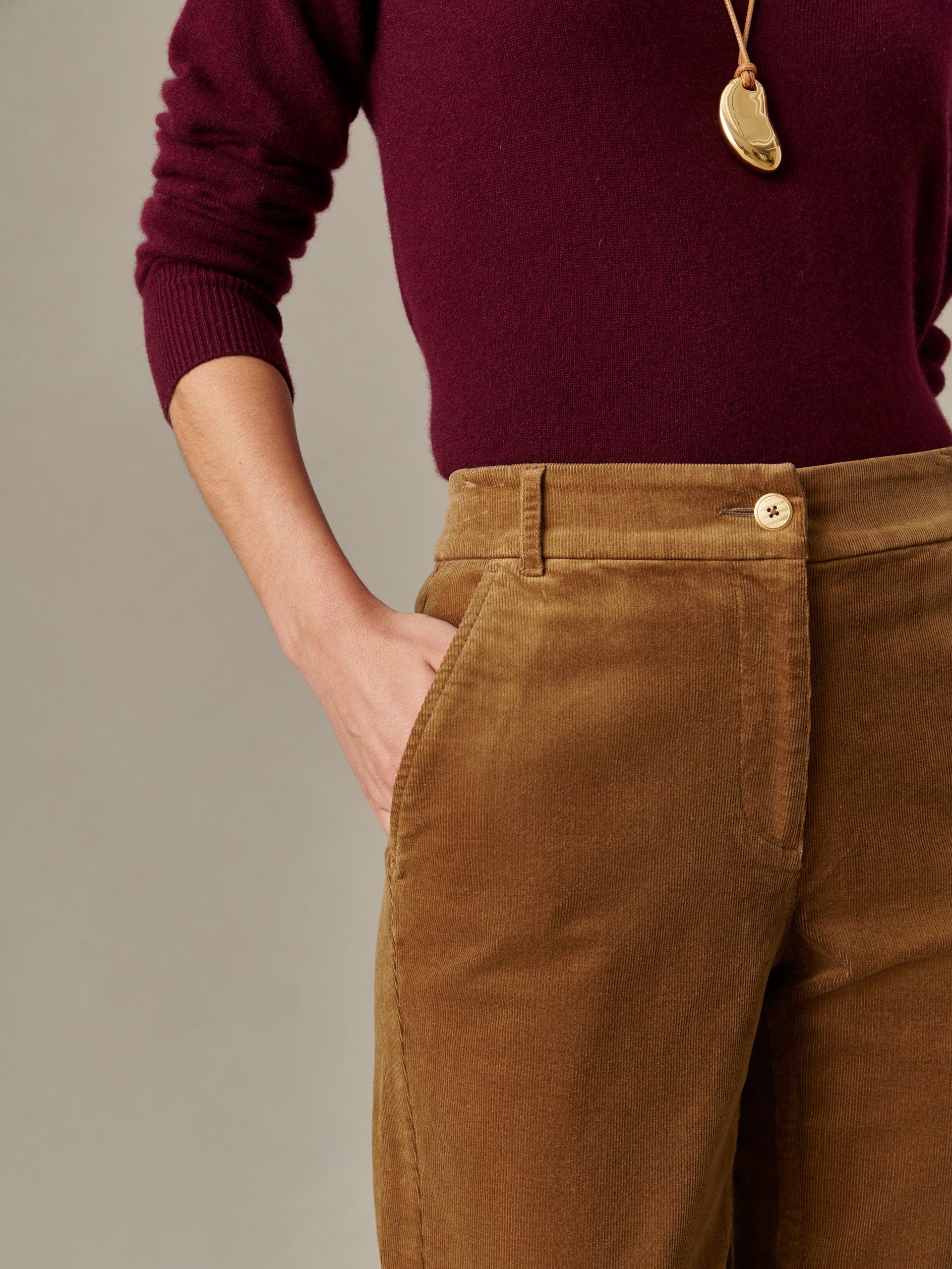 Close-up of a person wearing Avery Corduroy Pants in a warm brown tone paired with a burgundy sweater, showcasing J.McLaughlin's effortless style and enduring design quality.
