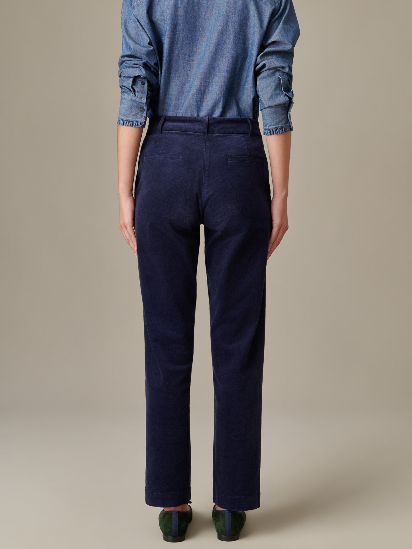 Rear view of a model wearing navy Avery Corduroy Pants by J.McLaughlin, paired with a rolled-up sleeve chambray shirt and dark shoes, showcasing timeless style and craftsmanship.