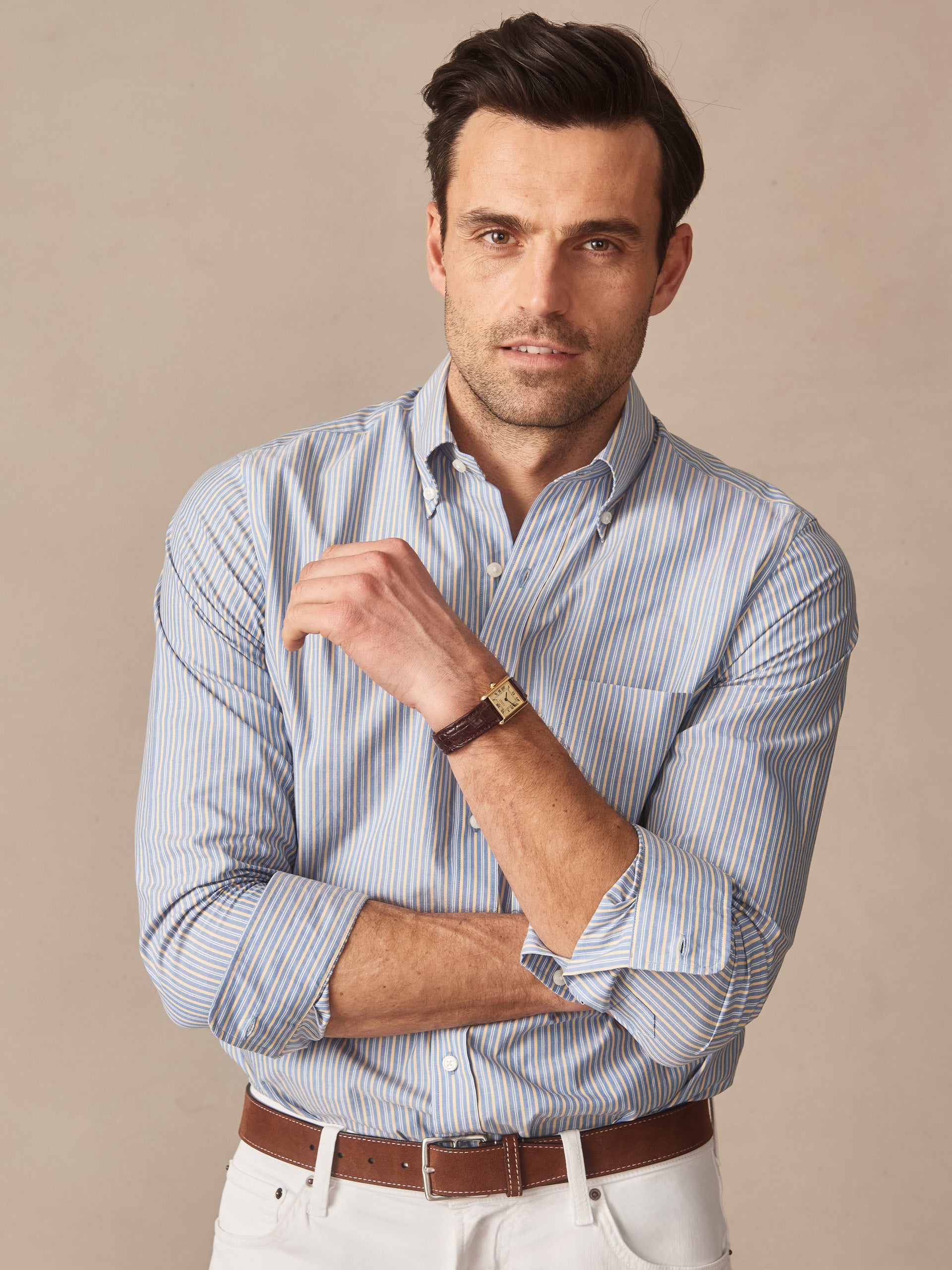 Man wearing a Belvedere Cotton Shirt in Multi Stripe by J.McLaughlin, paired with white pants and a brown leather belt, showcasing effortlessly stylish, enduring designs with innovative fabrics.