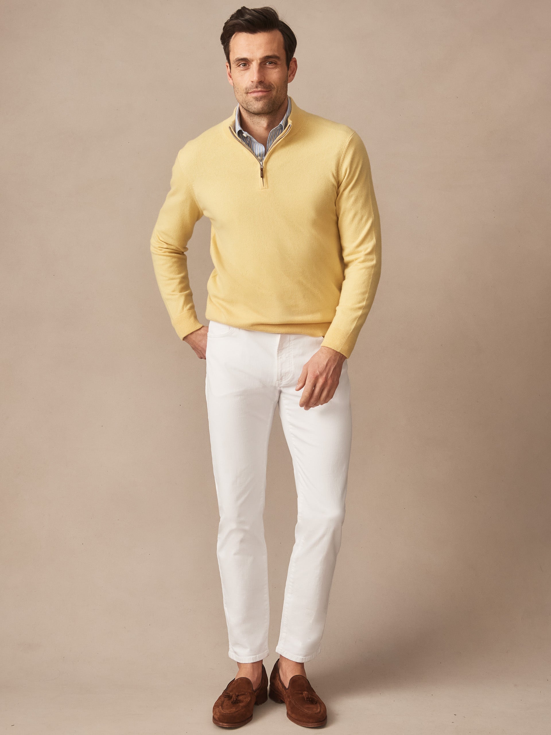 Man wearing a yellow Twain Cashmere 1/4 Zip sweater from J.McLaughlin paired with white pants and brown loafers, showcasing effortlessly stylish, enduring designs and innovative fabrics.