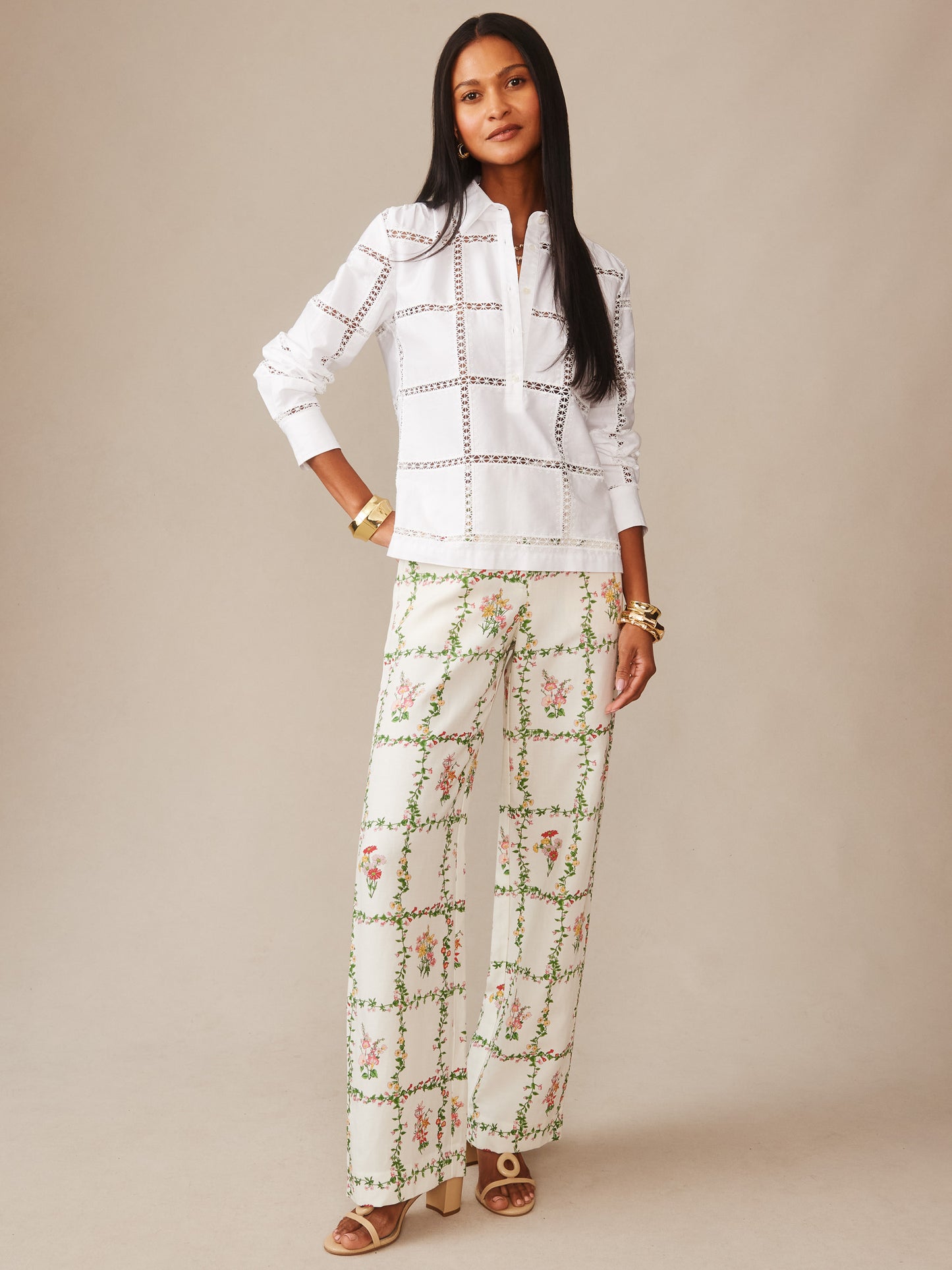 A model wears the Kyla Embroidered Shirt by J.McLaughlin, featuring a white base with delicate cut-out detailing paired with floral patterned wide-leg pants, showcasing effortlessly stylish, enduring designs.