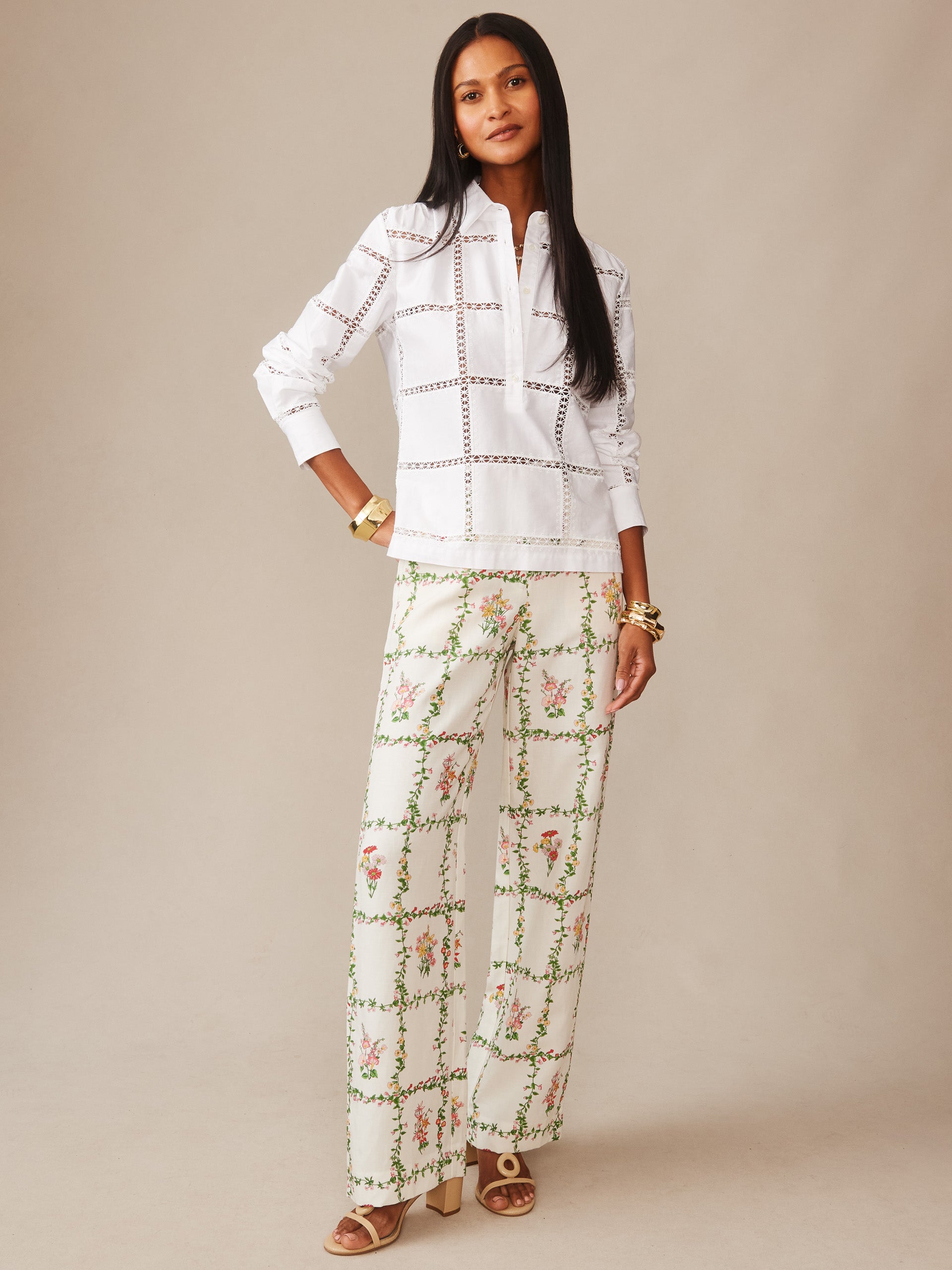 A model wears the Kyla Embroidered Shirt by J.McLaughlin, featuring a white base with delicate cut-out detailing paired with floral patterned wide-leg pants, showcasing effortlessly stylish, enduring designs.