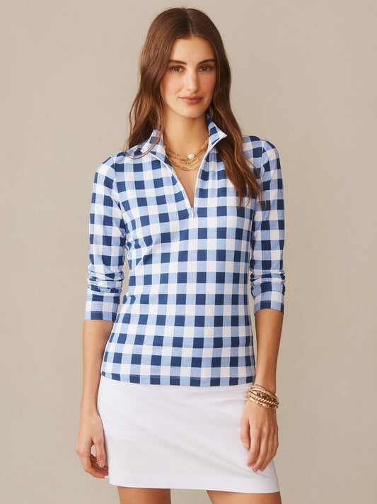 A woman wearing a J. McLaughlin Bedford Top in Textured Gingham featuring a blue and white checkered pattern with long sleeves and a zip collar, styled with layered necklaces and a white skirt, showcasing effortlessly stylish, enduring designs with innovative fabrics and a legacy of timeless fashion. A destination for defining style. Life, Well-Lived.