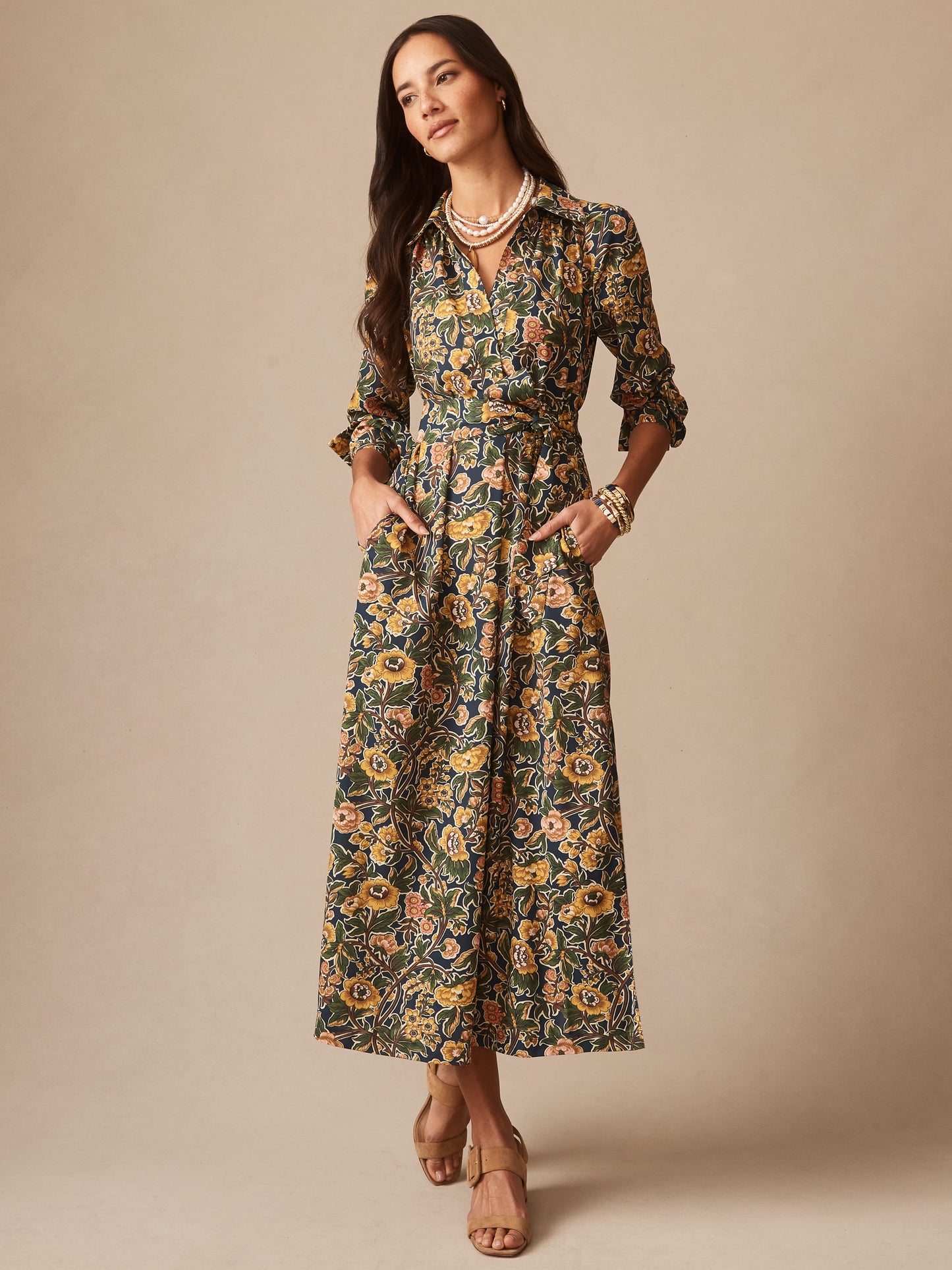 Woman wearing the Belle Dress in Bucolic Blooms by J.McLaughlin, a floral long-sleeve dress featuring a belted waist, styled with layered necklaces and heeled sandals, effortlessly stylish and embodying enduring designs and innovative fabrics. A destination for defining style. Life, Well-Lived.