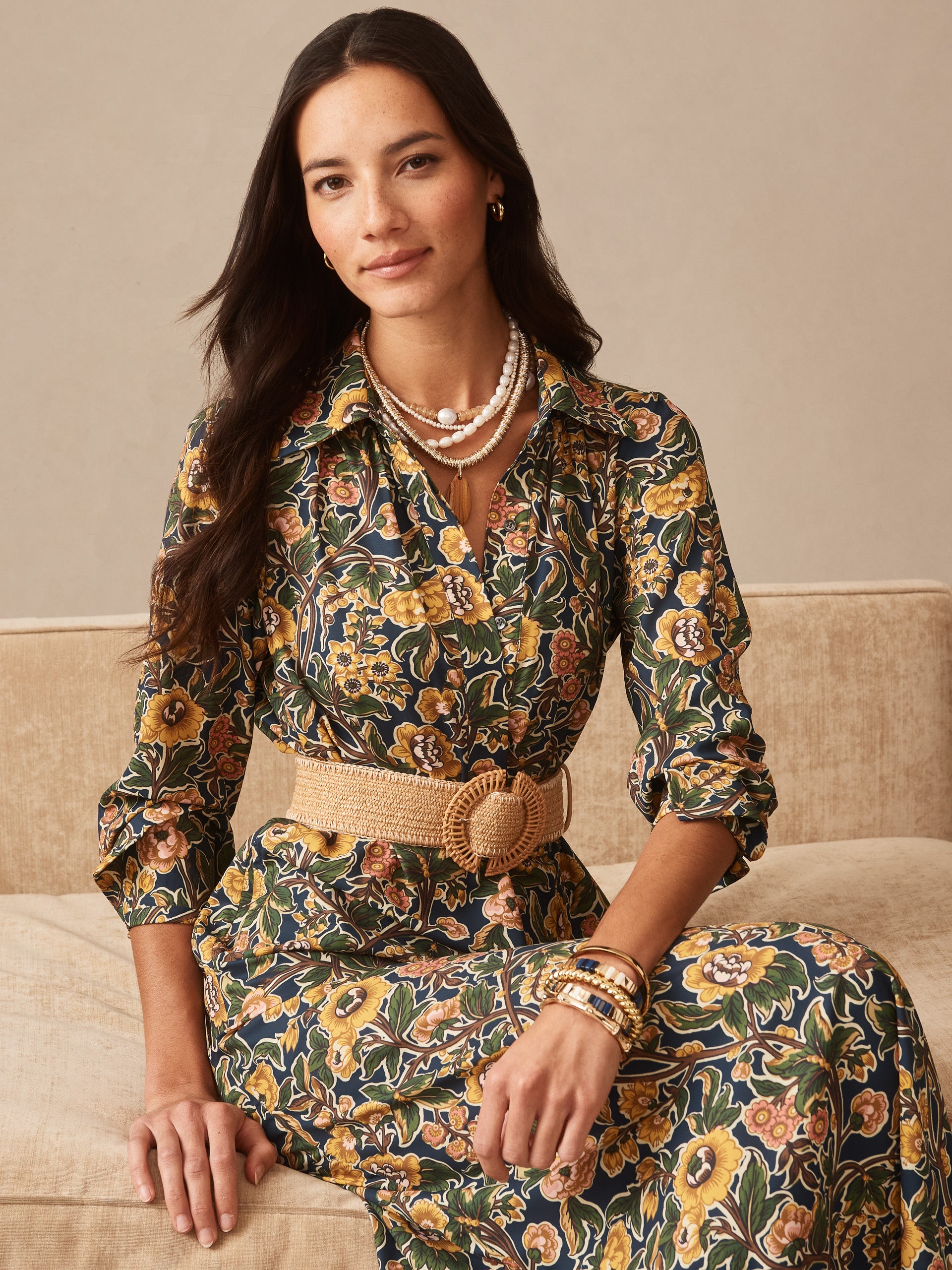 Woman wearing the Belle Dress in Bucolic Blooms by J.McLaughlin, featuring a floral pattern in earthy tones, styled with layered pearl necklaces, gold earrings, and a woven belt, embodying effortlessly stylish, enduring designs and innovative fabrics—A destination for defining style. Life, Well-Lived.