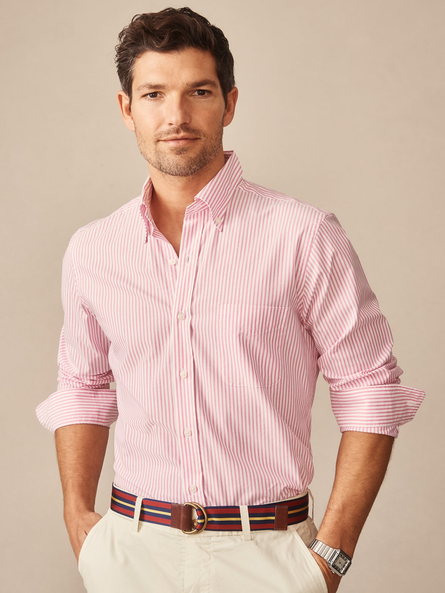 A man wearing the Belvedere Cotton Shirt in Bengal Stripe by J.McLaughlin, featuring effortlessly stylish pink and white stripes, paired with a striped belt, showcasing enduring designs and innovative fabrics for a life well-lived.