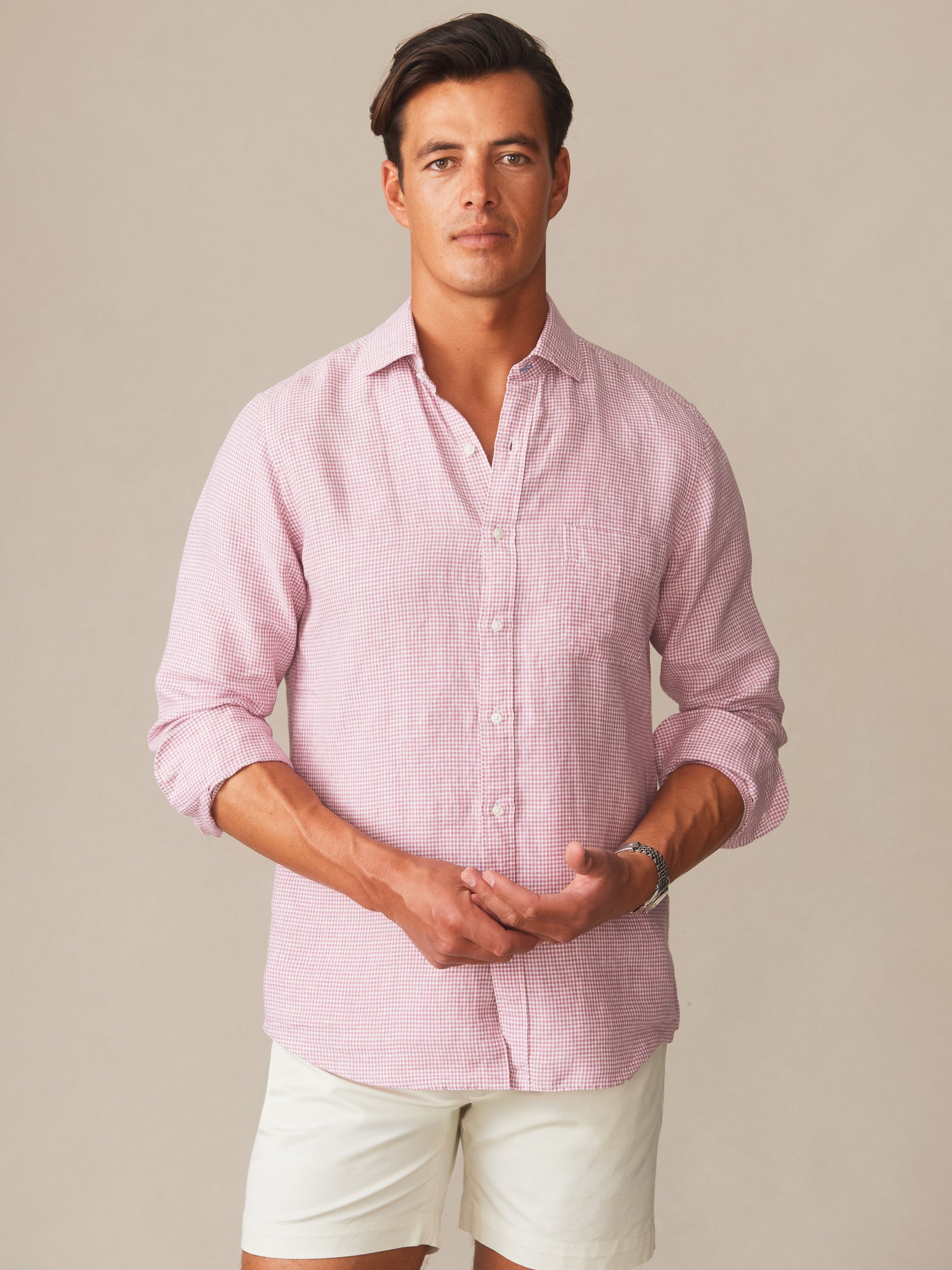 Man wearing a pink and white Gramercy Linen Shirt in Micro Gingham by J.McLaughlin, paired with white shorts, showcasing effortlessly stylish, enduring designs with innovative fabrics.