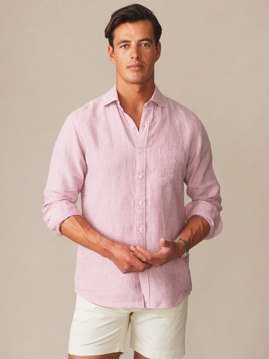 Man wearing a pink and white Gramercy Linen Shirt in Micro Gingham by J.McLaughlin, paired with white shorts, showcasing effortlessly stylish, enduring designs with innovative fabrics.