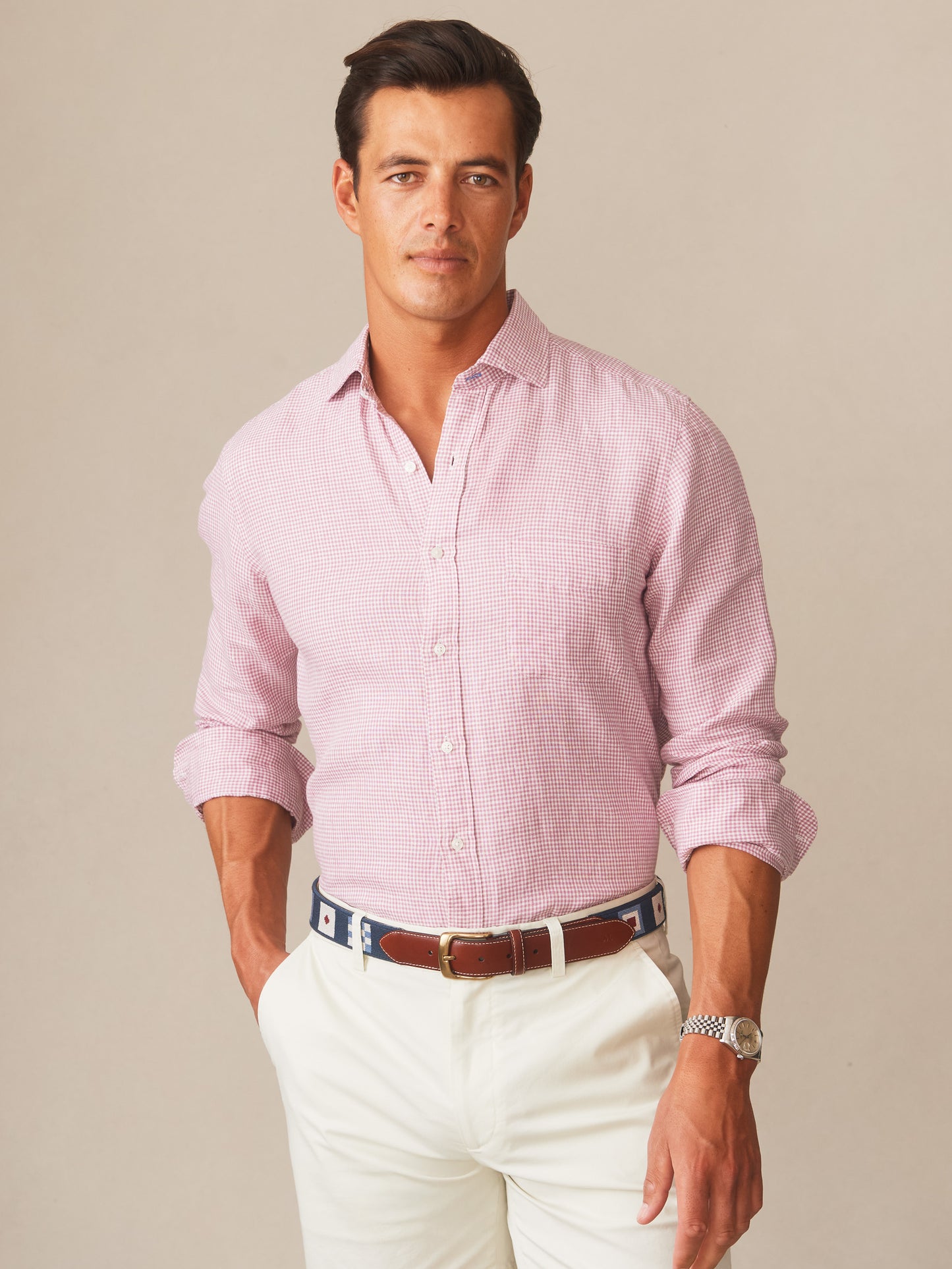 Man wearing a pink and white micro gingham button-down shirt paired with white pants and a navy belt, showcasing the Gramercy Linen Shirt in Micro Gingham by J.McLaughlin, effortlessly stylish and enduring designs for a destination defining style. Life, Well-Lived.