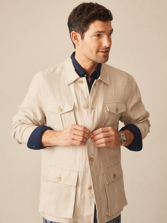 Man wearing a beige Aston Linen Safari Jacket in Herringbone by J.McLaughlin over a navy shirt, showcasing effortlessly stylish, enduring designs with innovative fabrics in timeless fashion.