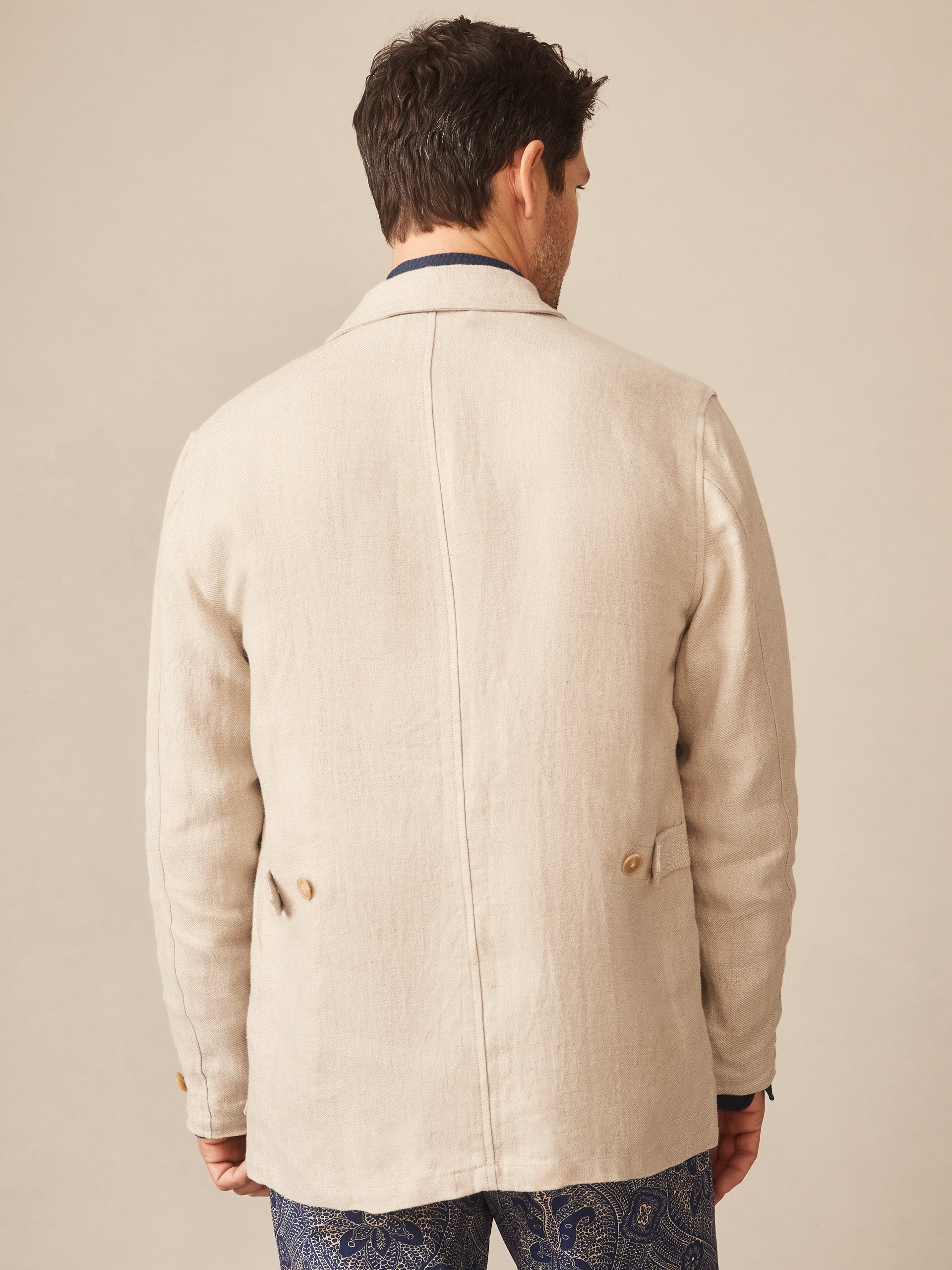 Man seen from behind wearing an Aston Linen Safari Jacket in Herringbone by J.McLaughlin, showcasing effortlessly stylish tailoring with innovative fabrics and a legacy of timeless fashion.